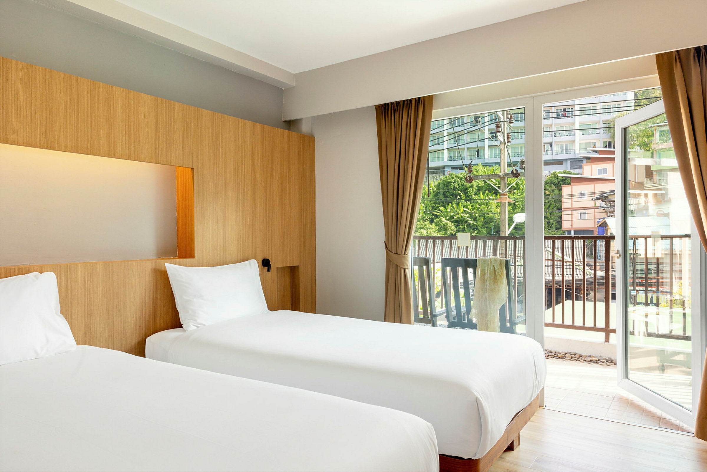 Två enkelsängar i ett hotellrum med stora glasdörrar mot en balkong. (AI-genererad text)