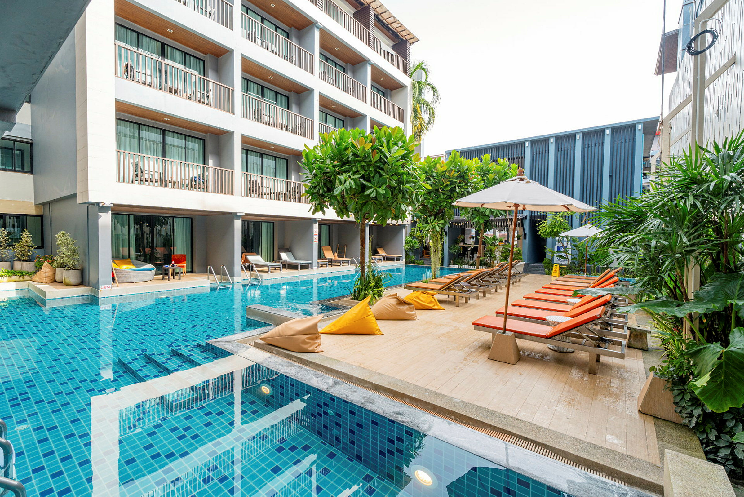 En modern hotellbyggnad intill en pool med solstolar och parasoller. (AI-genererad text)