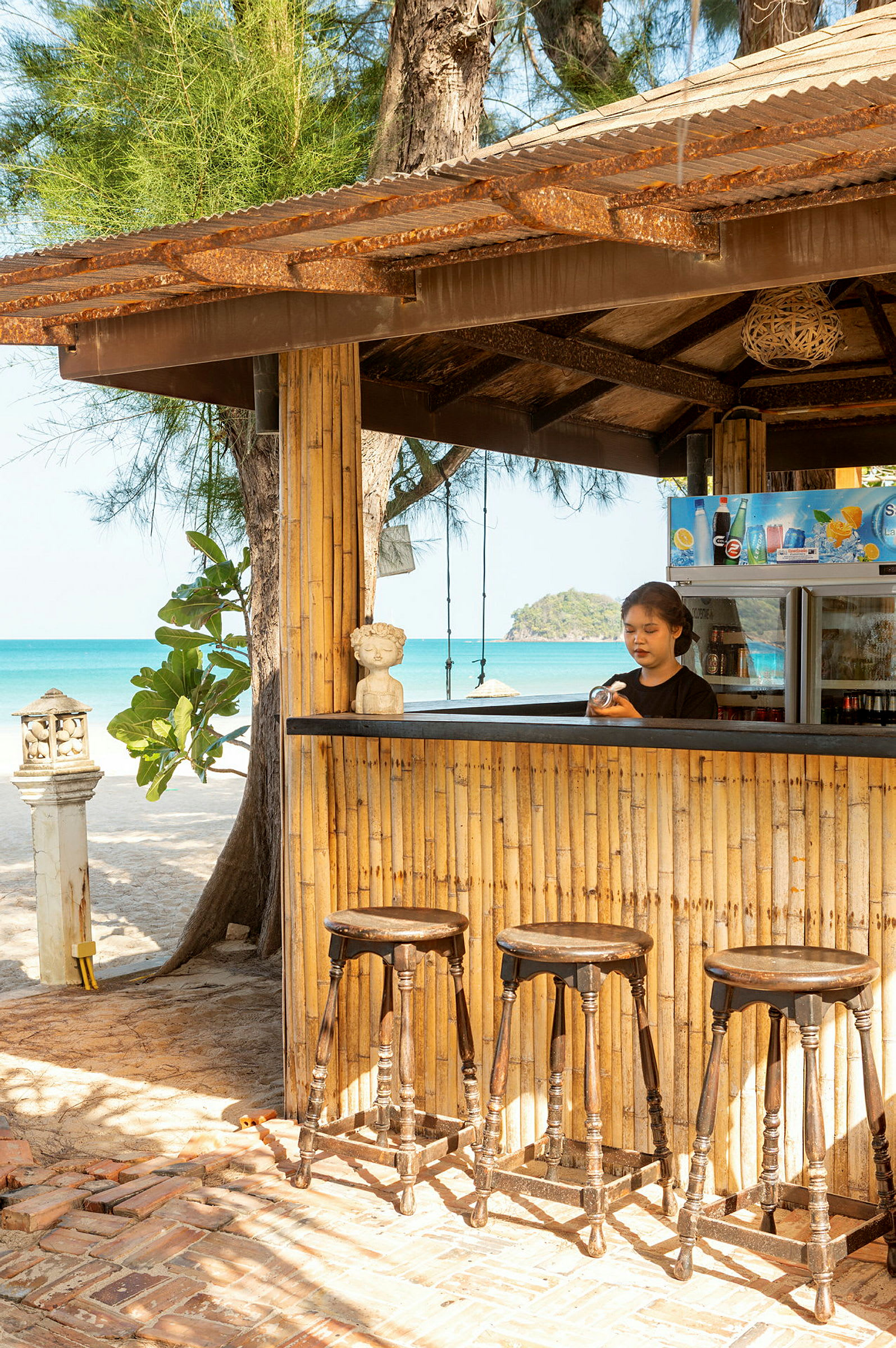 En bar med bambuväggar, träpallar och strand i bakgrunden. (AI-genererad text)