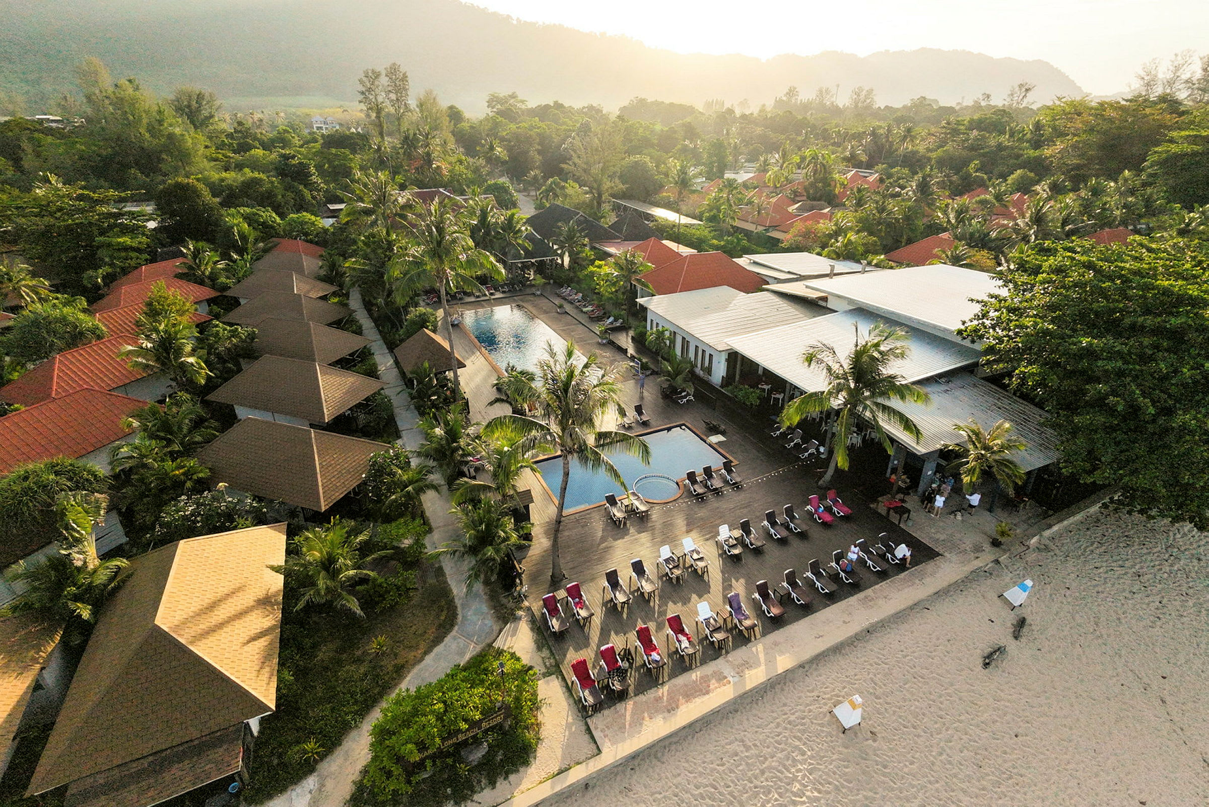 Luftbild av en resort med pool, solstolar och omgivande vegetation nära en strand. (AI-genererad text)