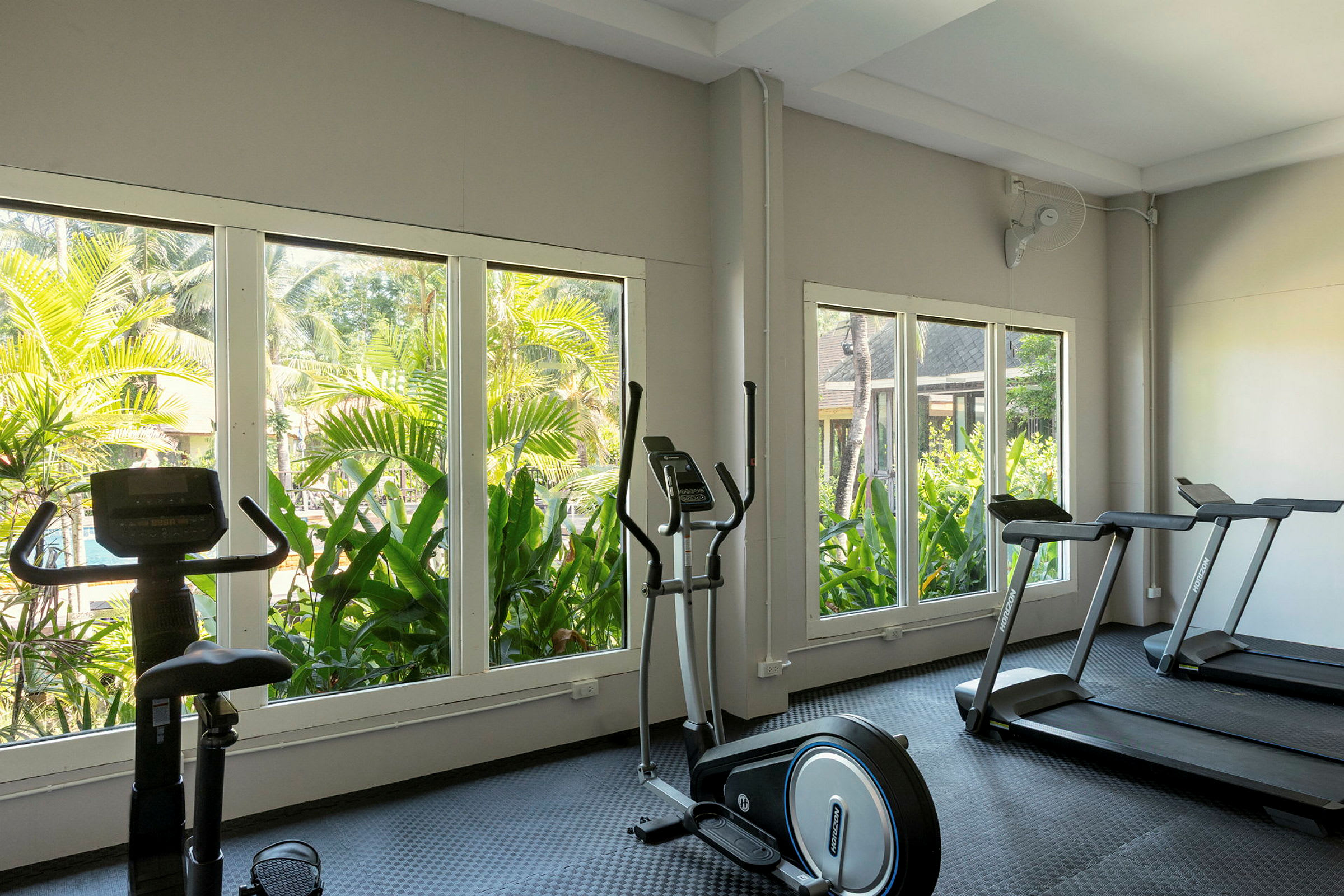 Ett gym med träningsmaskiner och stora fönster som visar utsikt över grönska. (AI-genererad text)