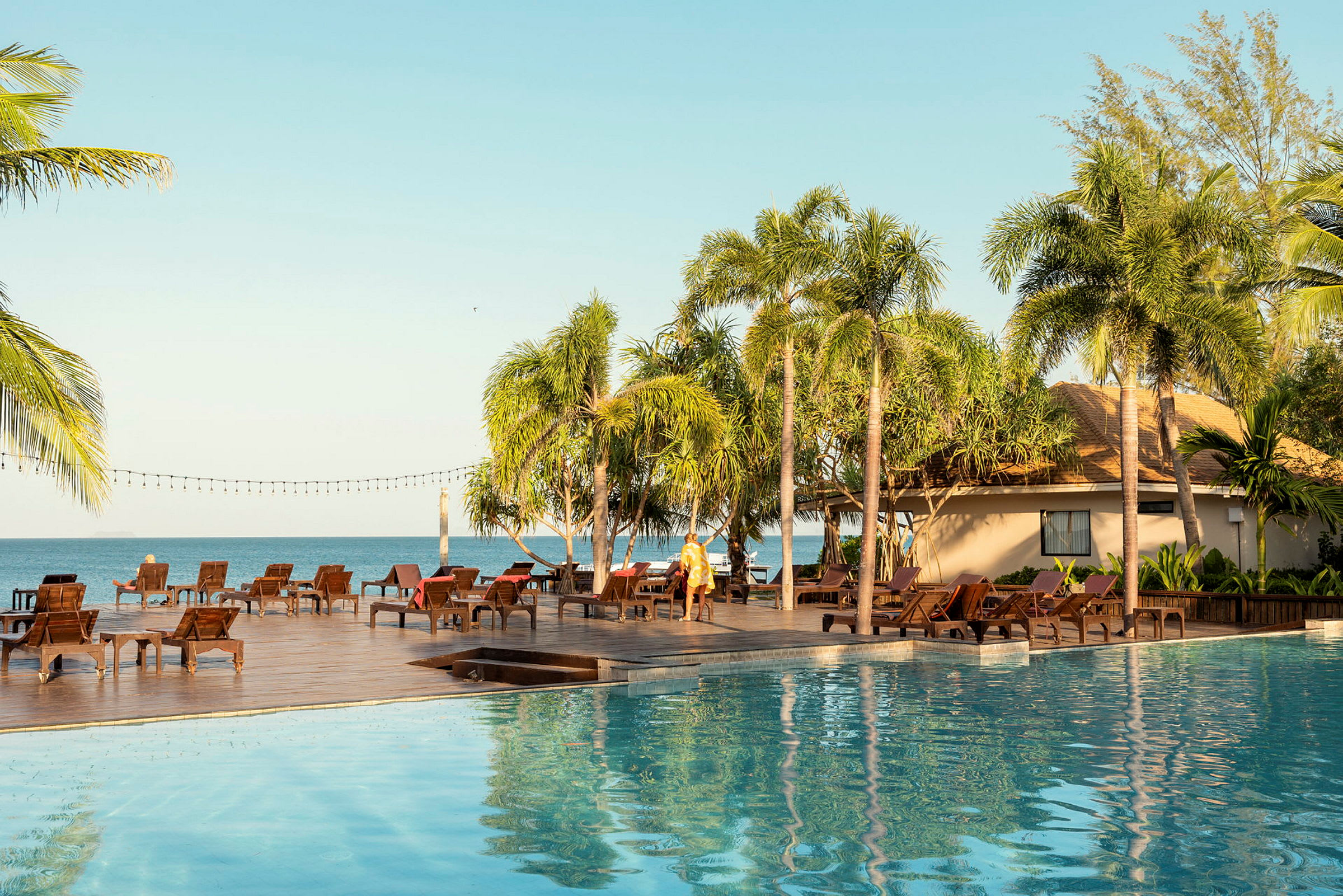 En solig resort med pool, solsängar, palmträd och ett hav i bakgrunden. (AI-genererad text)