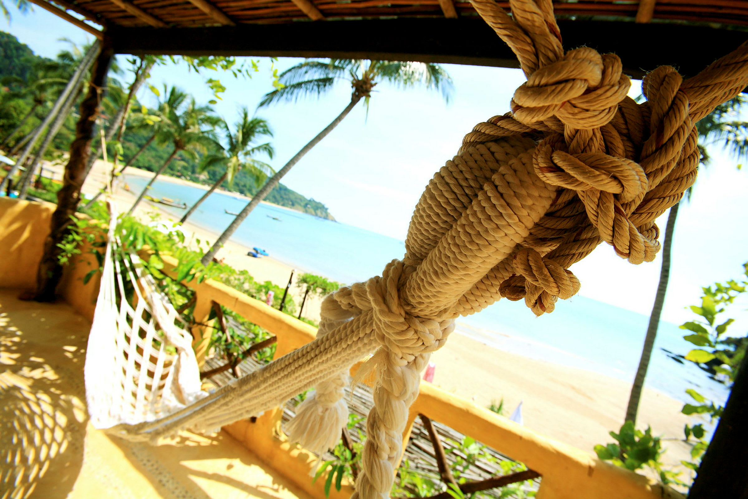 Bild av en hammock i ett träskydd på en terrass med utsikt över en strand och palmer. (AI-genererad text)