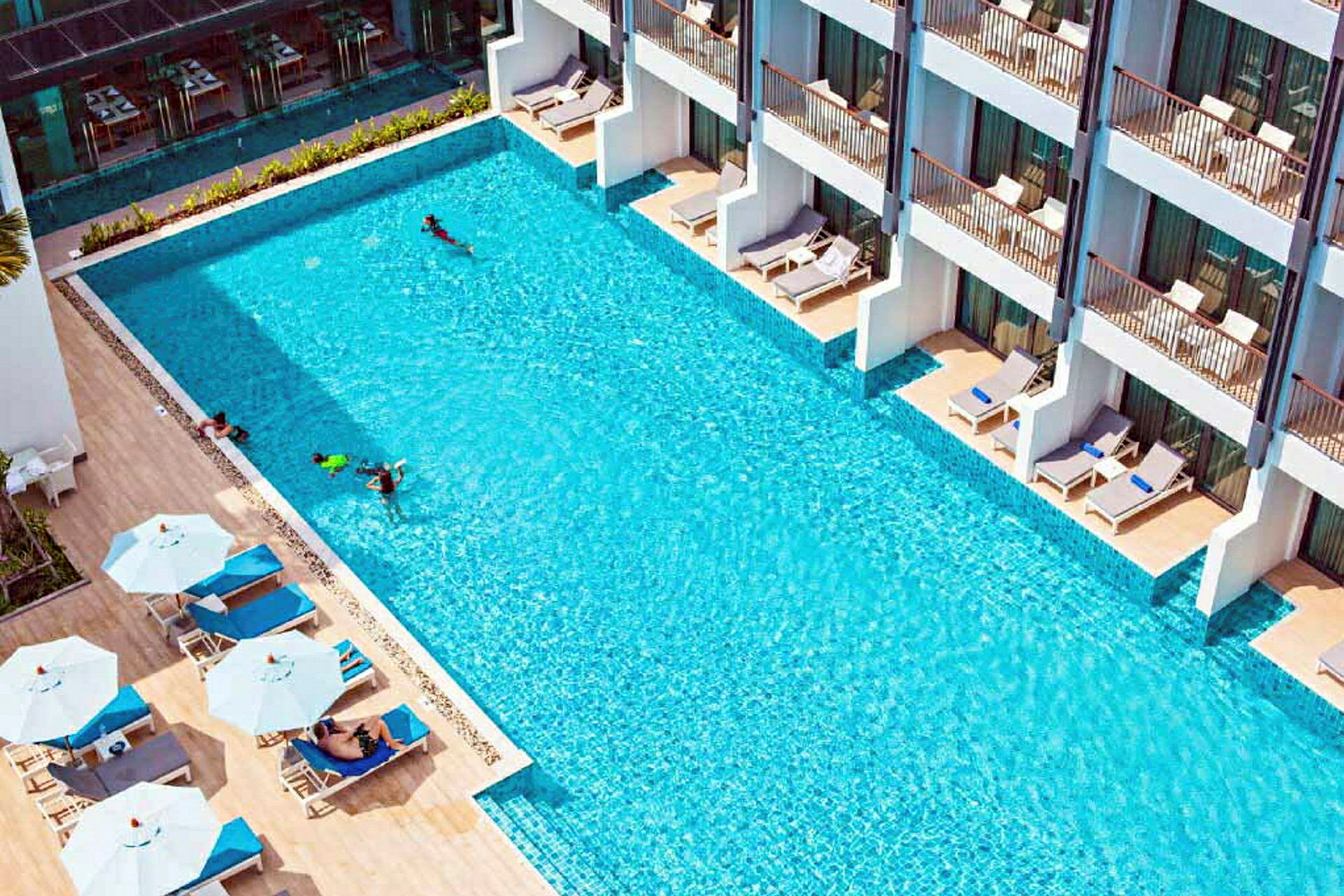En utomhuspool med solstolar och parasoller vid sidan om samt byggnader med terrasser. (AI-genererad text)