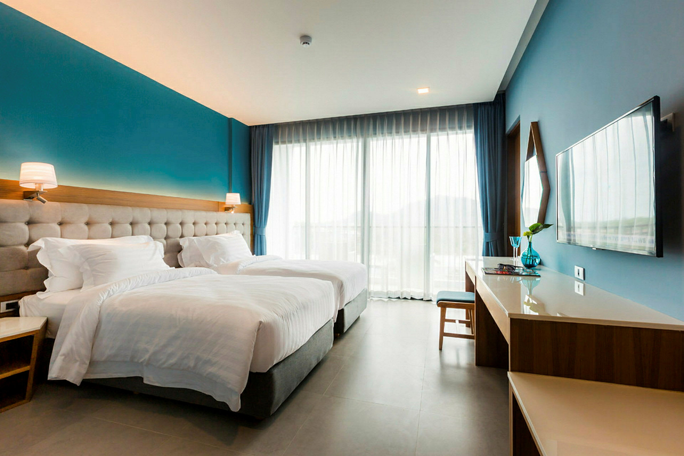 Hotellrum med två enkelsängar, skrivbord, TV och stora fönster. (AI-genererad text)