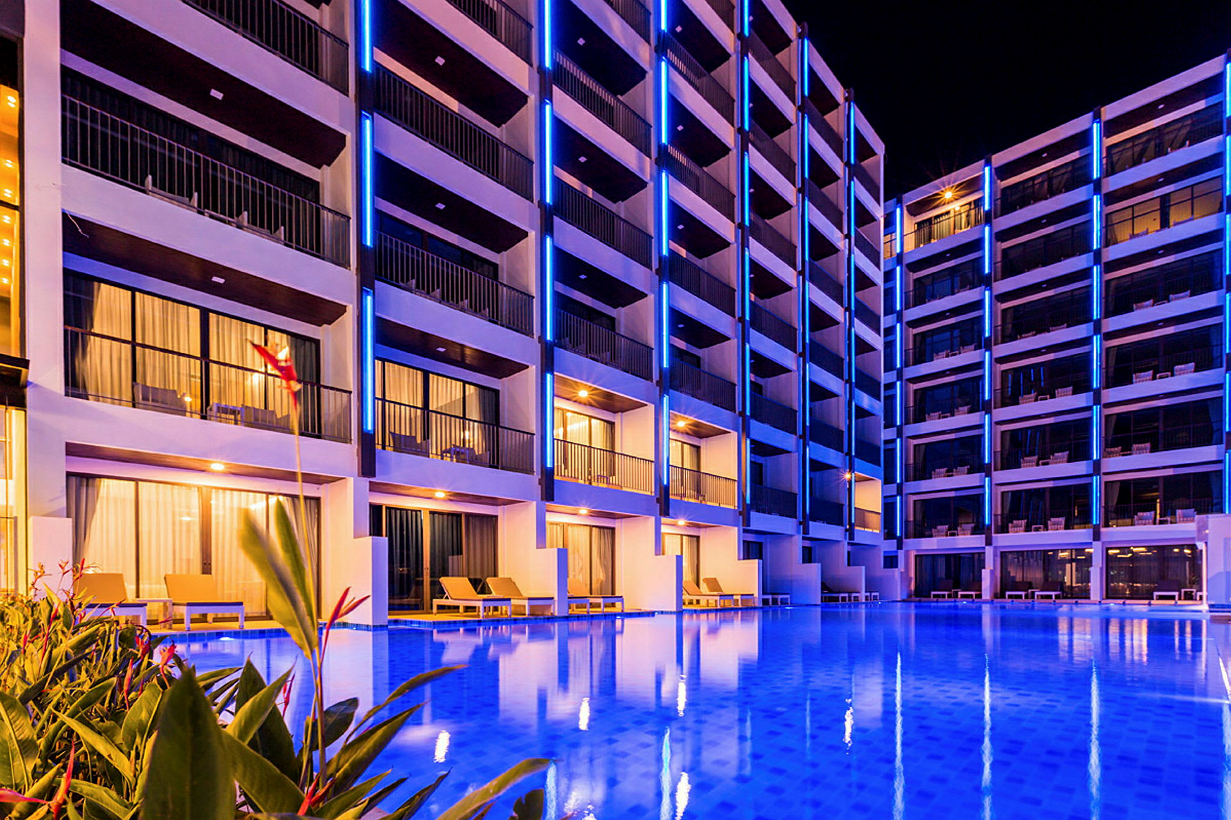 En bild av ett hotell med flera våningar, upplyst med blå neonljus och en pool i förgrunden. (AI-genererad text)