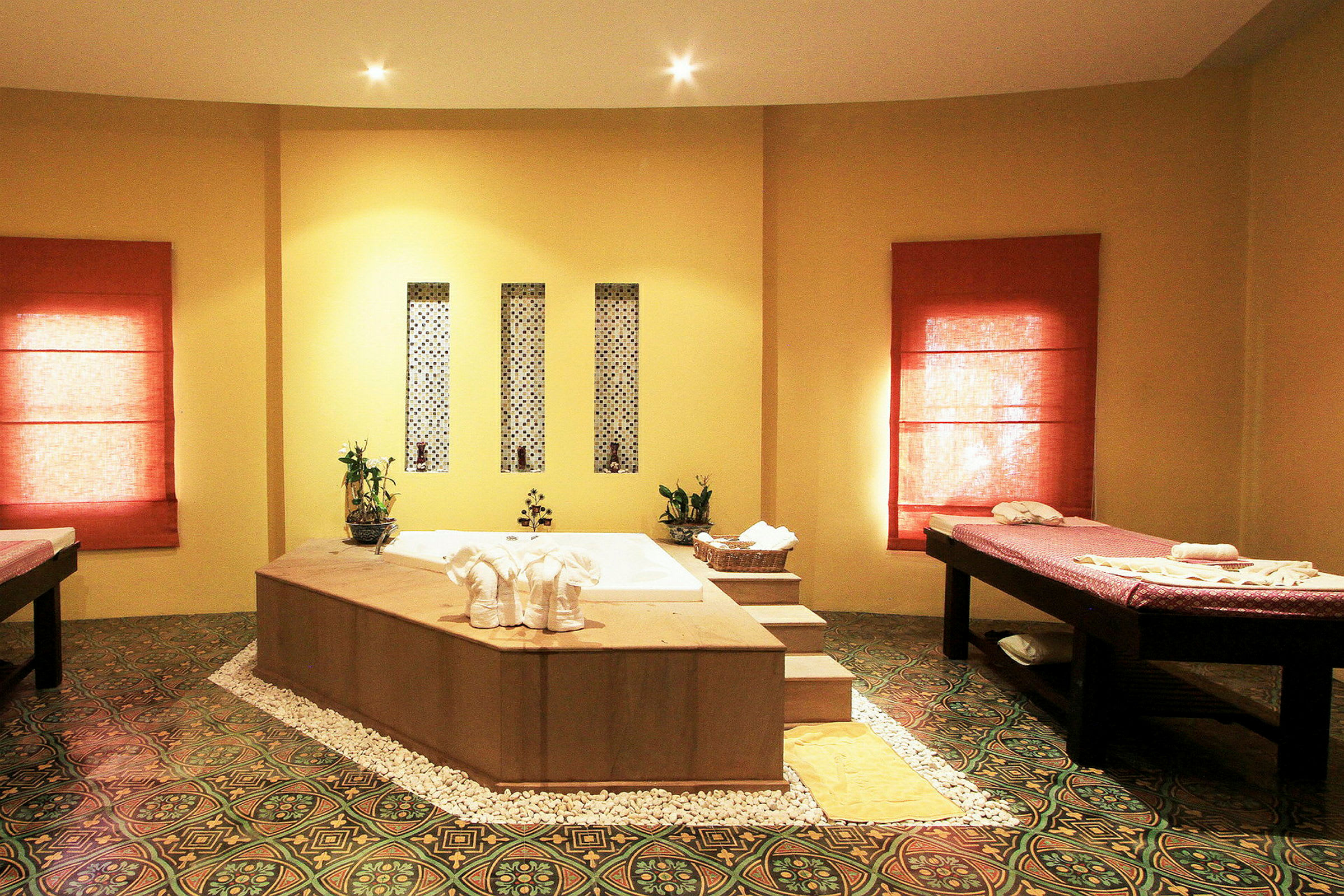 Spa-rum med badkar i centrum, massagebänkar och dekorativa element. (AI-genererad text)