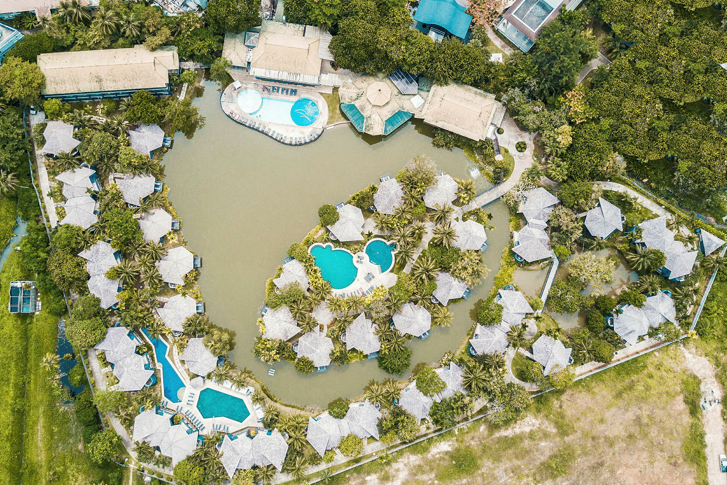 Fågelperspektiv av ett semesteranläggning med bungalower, pooler och grönområden. (AI-genererad text)