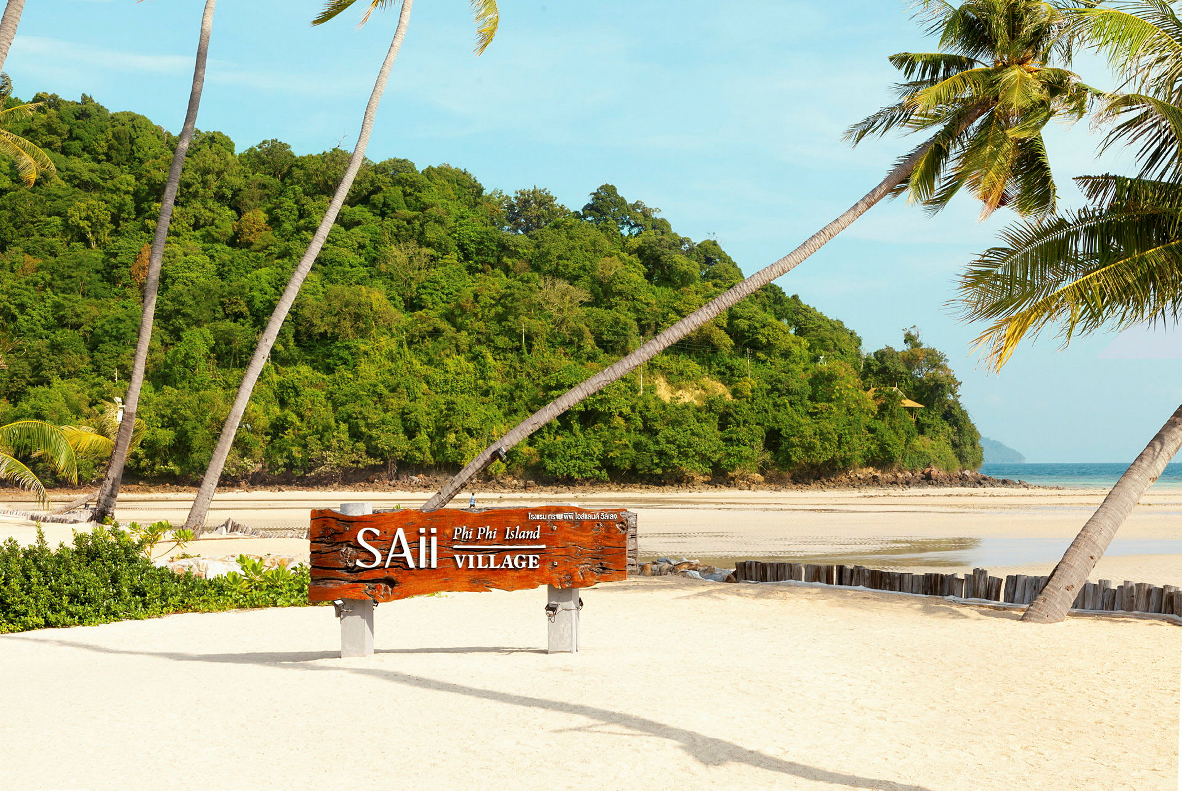 Sandstrand med palmer och en träskylt som lyder "SAii Phi Phi Island Village", med grön vegetation och havet i bakgrunden. (AI-genererad text)