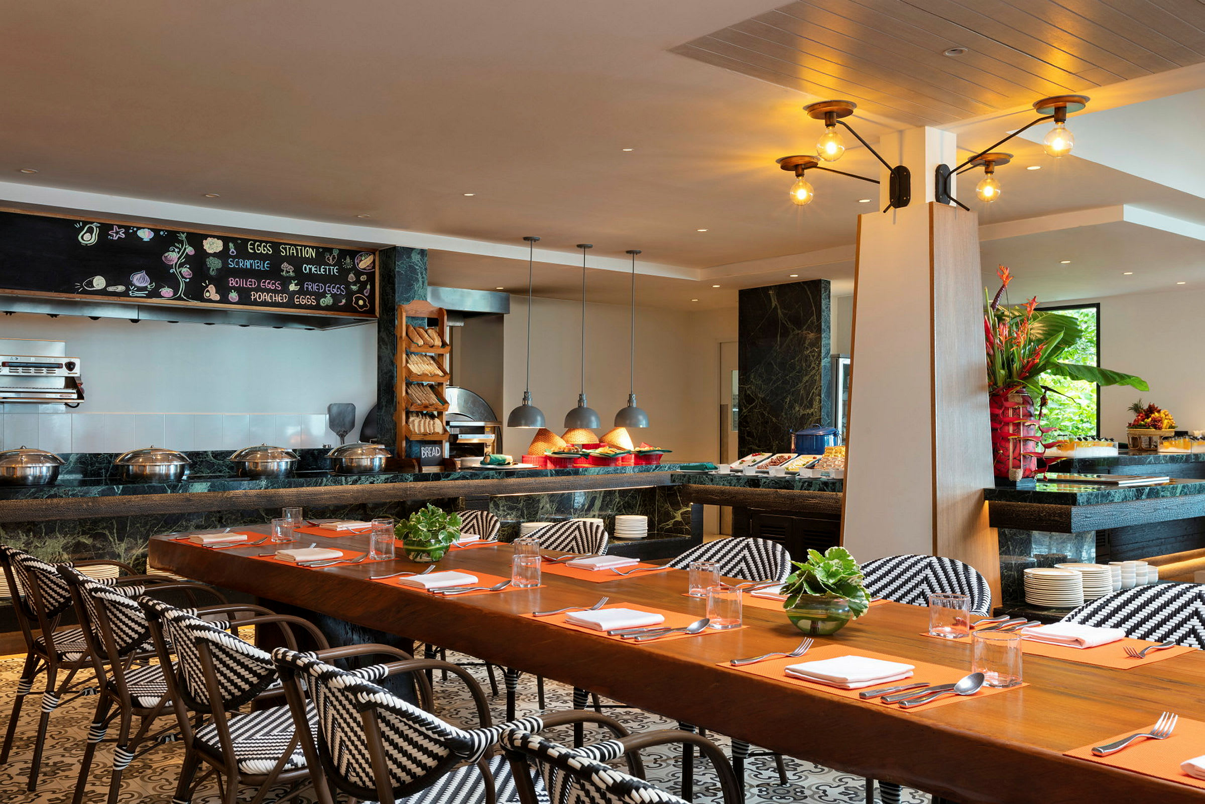 Interiör av en restaurang med ett långt matbord, stolar med mönstrade sitsar och en frukostbuffé med mat och dekorationer. (AI-genererad text)