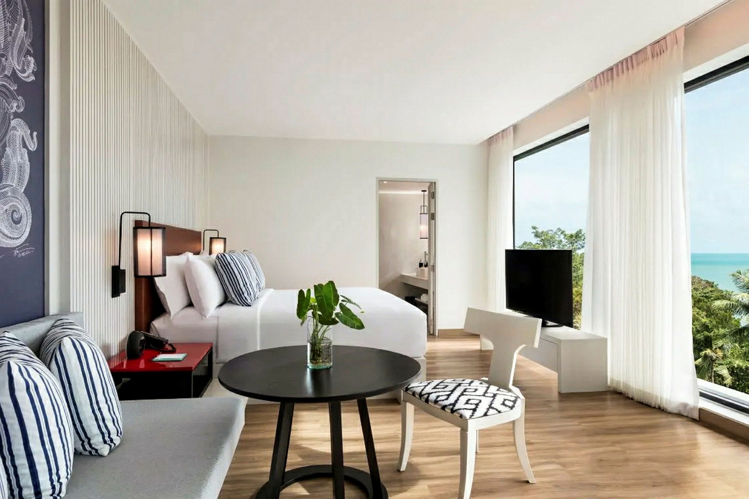 Ett ljust hotelrum med säng, sittgrupp, tv och utsikt över havet. (AI-genererad text)