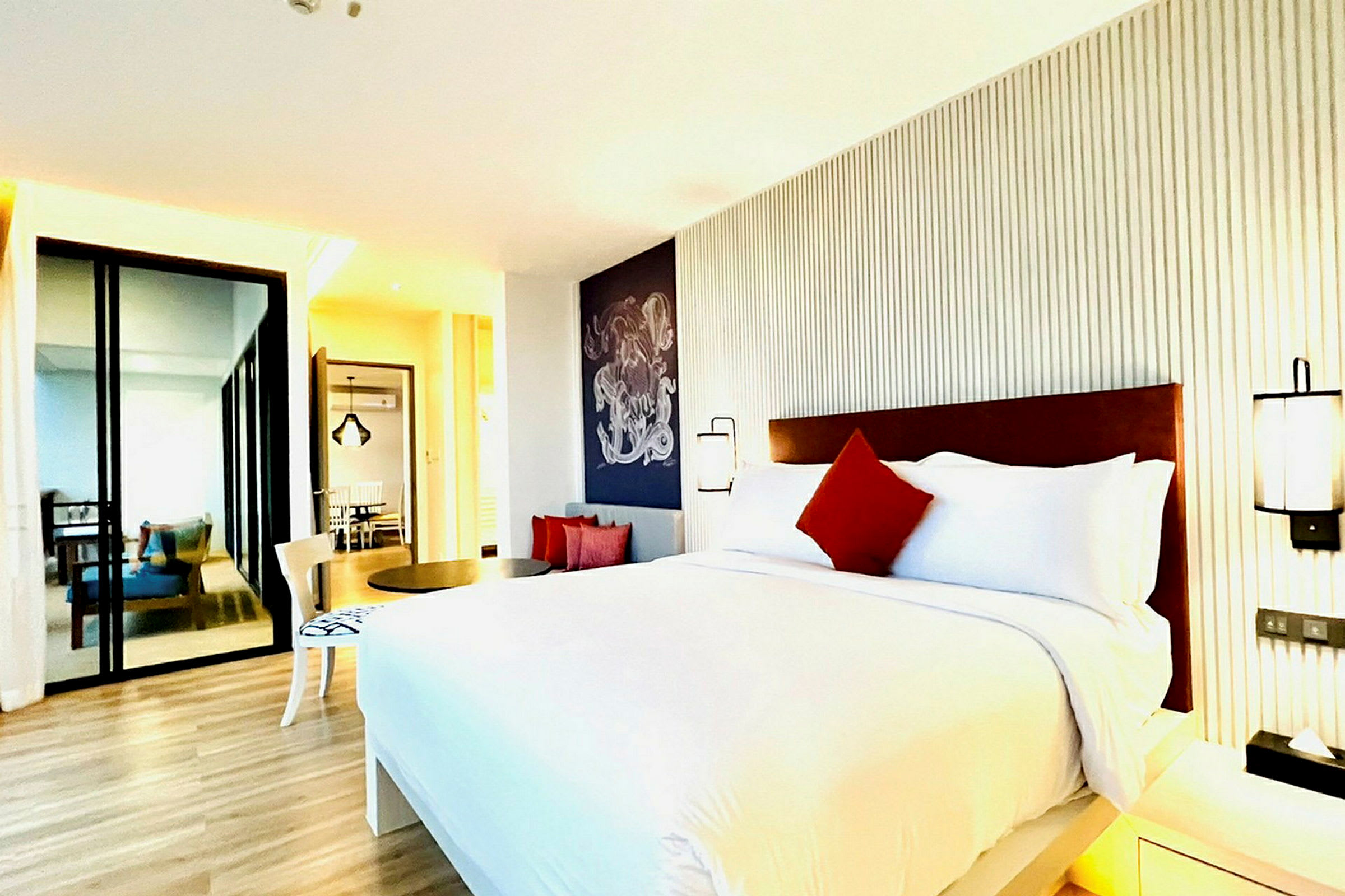 Ett modernt hotellrum med en stor säng, vita och röda kuddar, minimalistisk inredning och trägolv. (AI-genererad text)