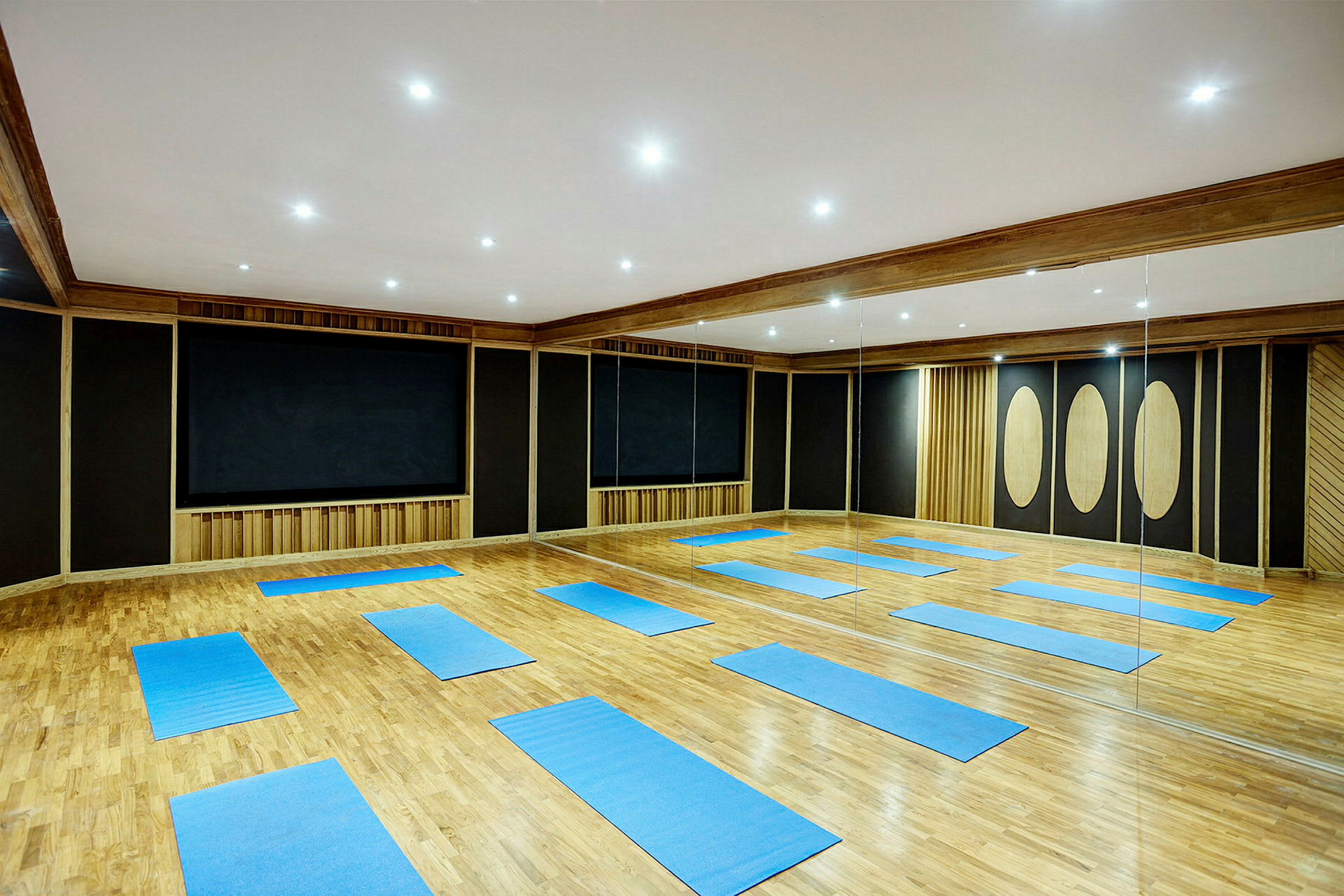 Ett träningsrum med parkettgolv, blå yogamattor placerade på golvet och spegelväggar. (AI-genererad text)