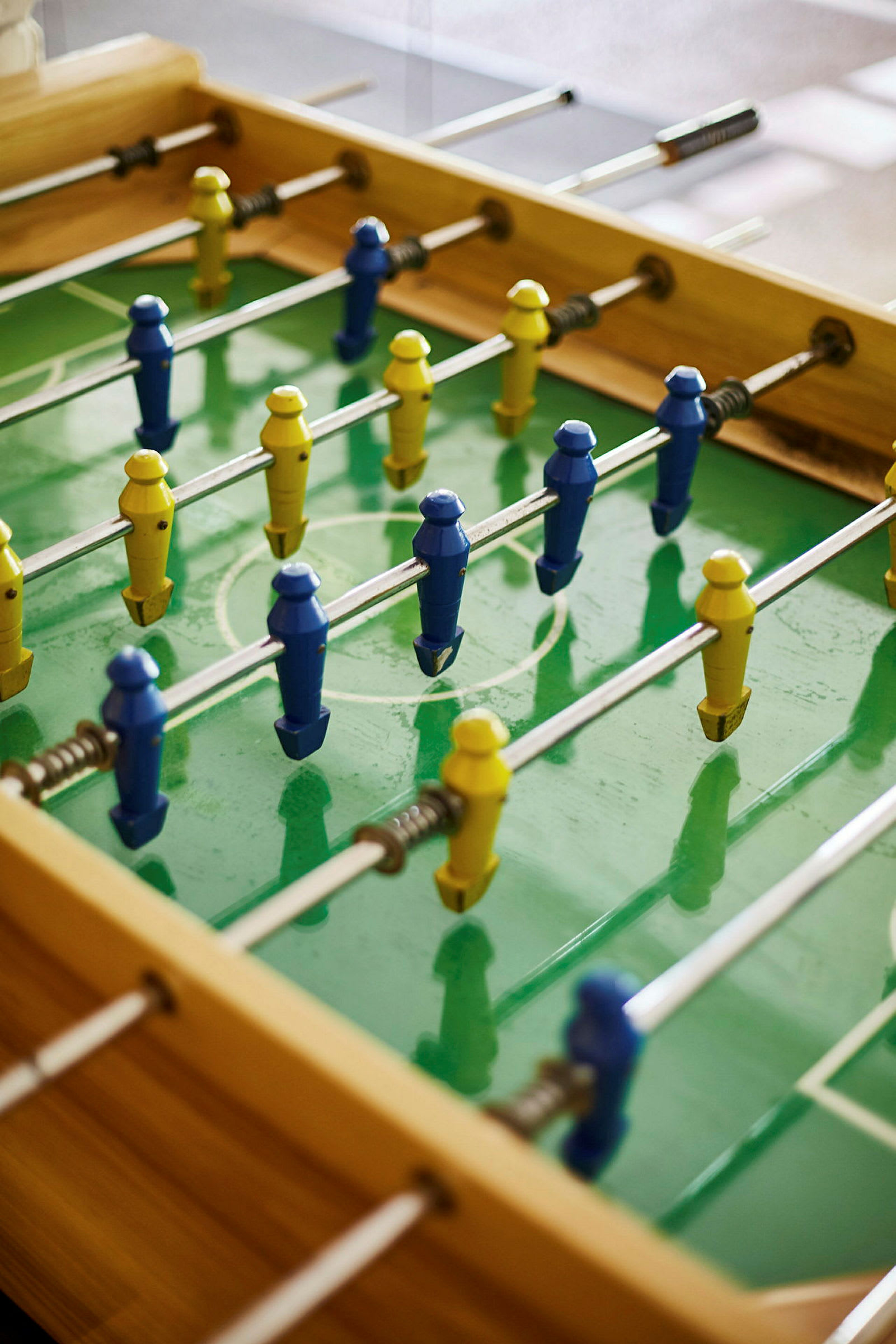 Ett foosballbord med plastfigurer i blåa och gula färger på grönt underlag. (AI-genererad text)