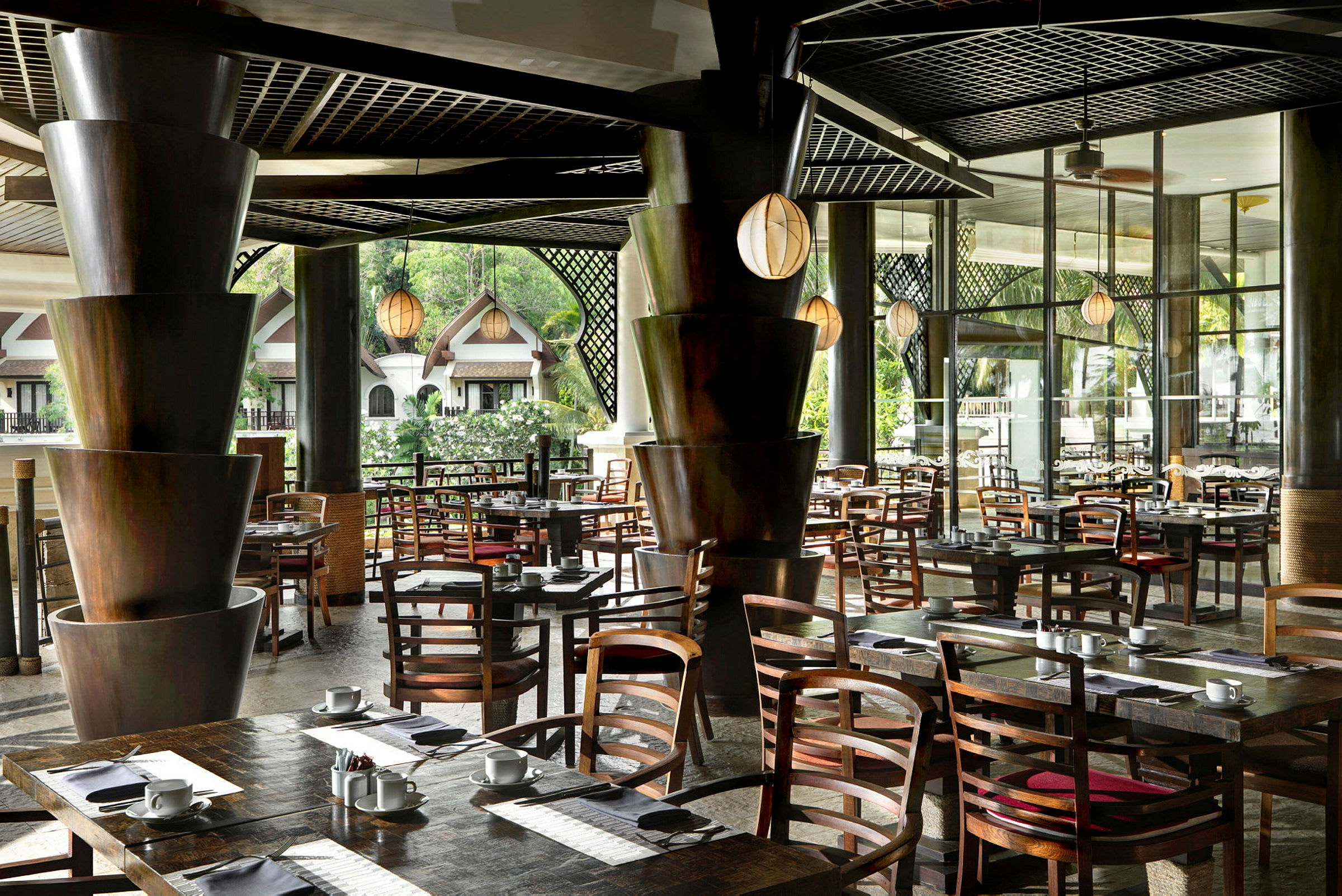 En modern restaurang med eleganta träbord och stolar, omgiven av grönska och stora fönster. (AI-genererad text)