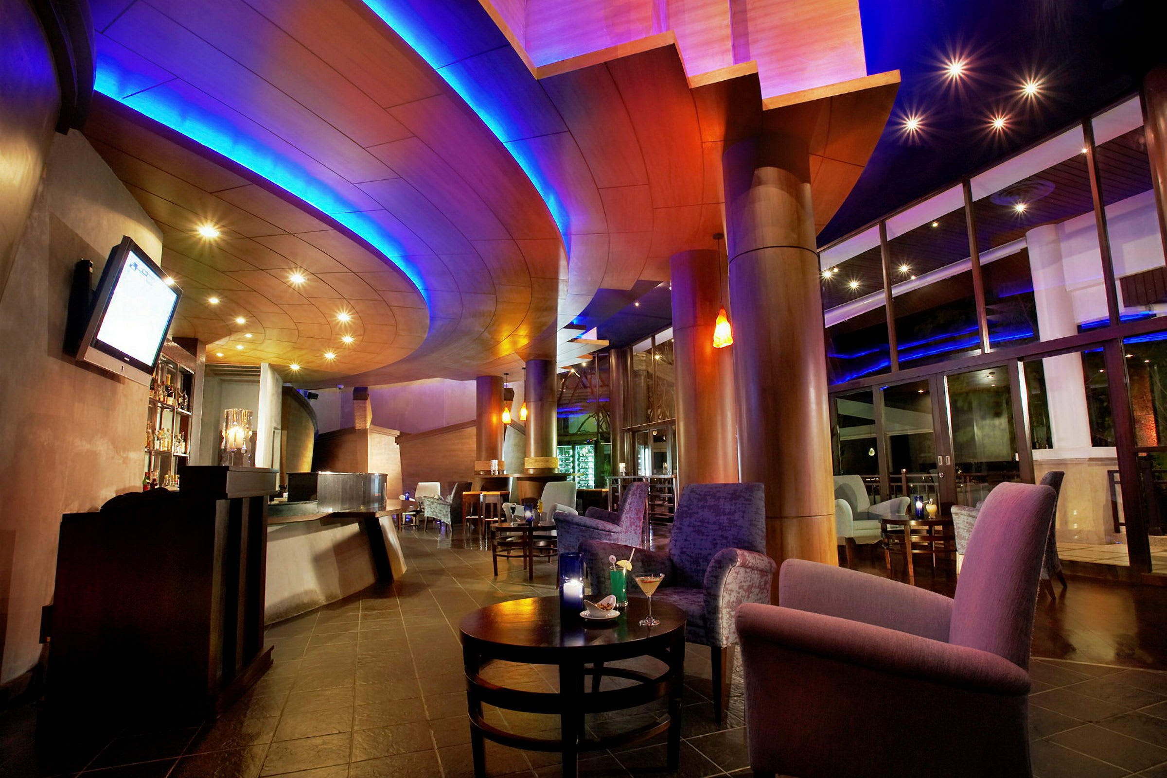 En interiör av en modern lounge eller bar med en välvd takdesign, mjuka fåtöljer och soffor, samt en snygg belysning i rummet. (AI-genererad text)