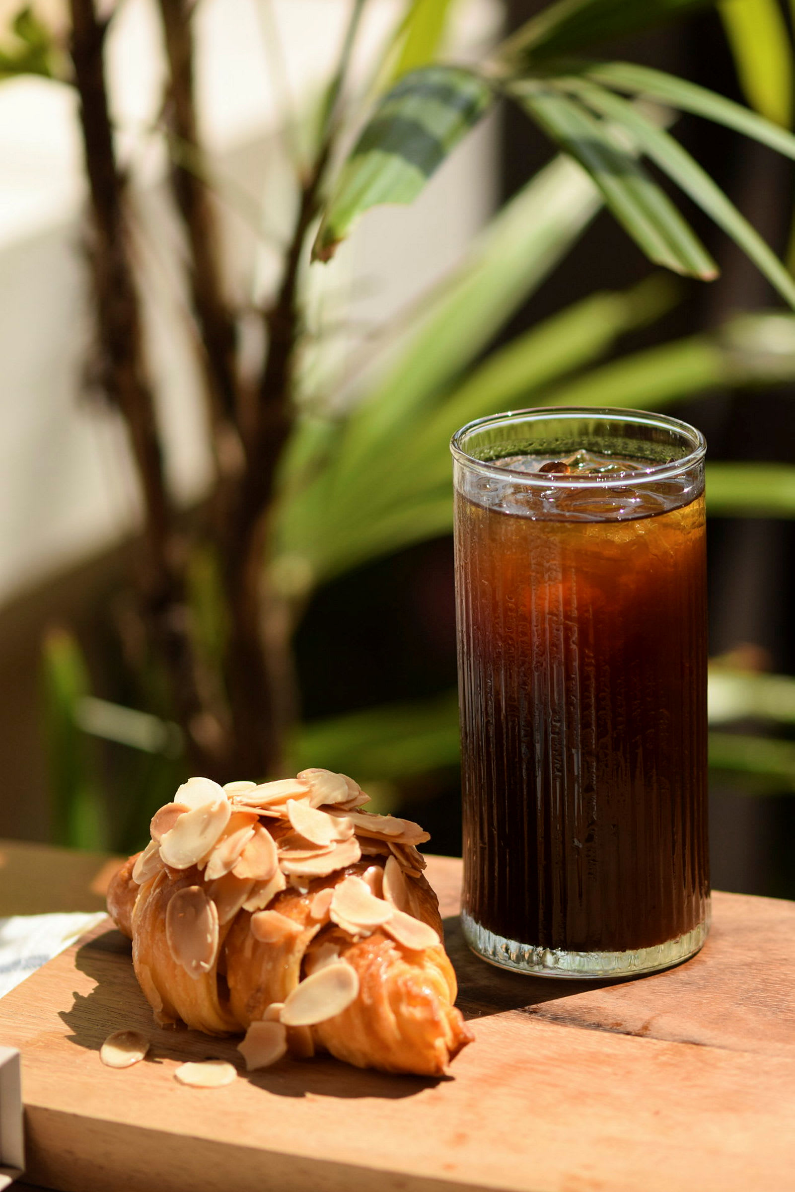Ett glas med kyld dryck och en croissant täckt med mandelflarn som står på ett träbord. (AI-genererad text)