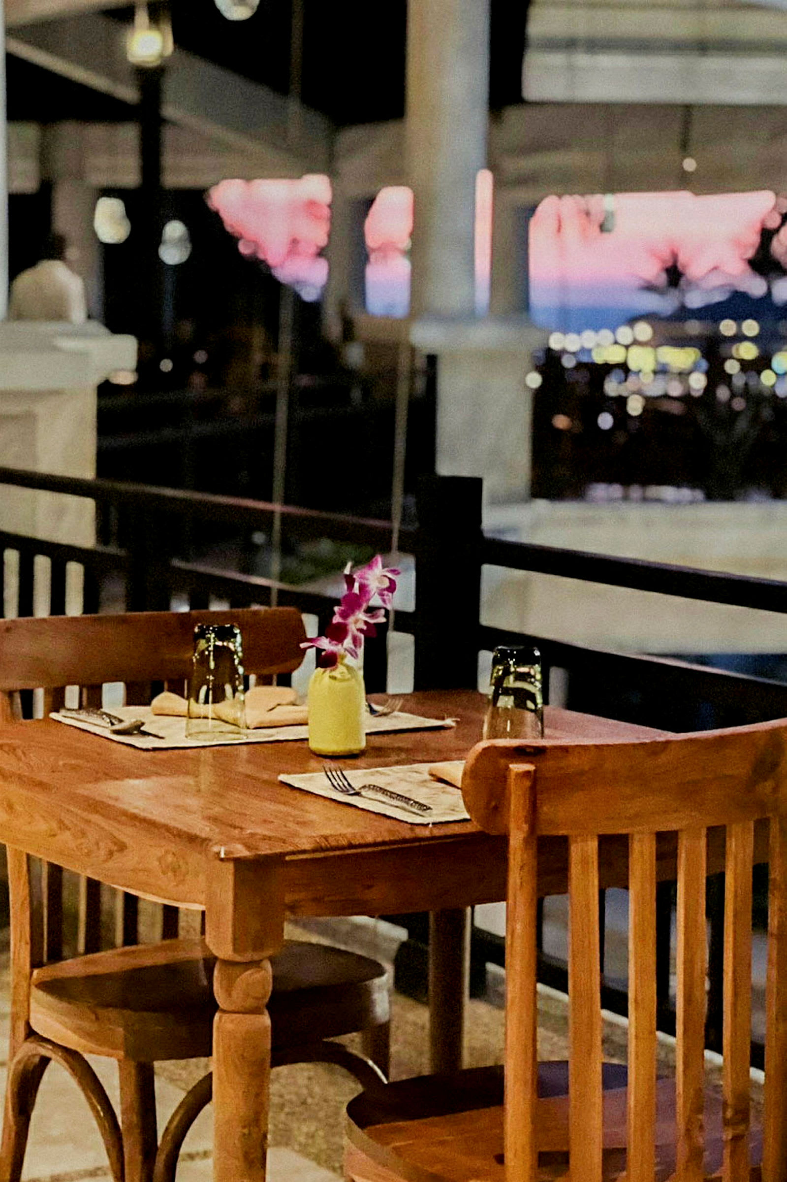 Ett dukat träbord med två stolar vid en restaurangterrass och bakgrund med suddigt utsikt över kvällslandskap. (AI-genererad text)