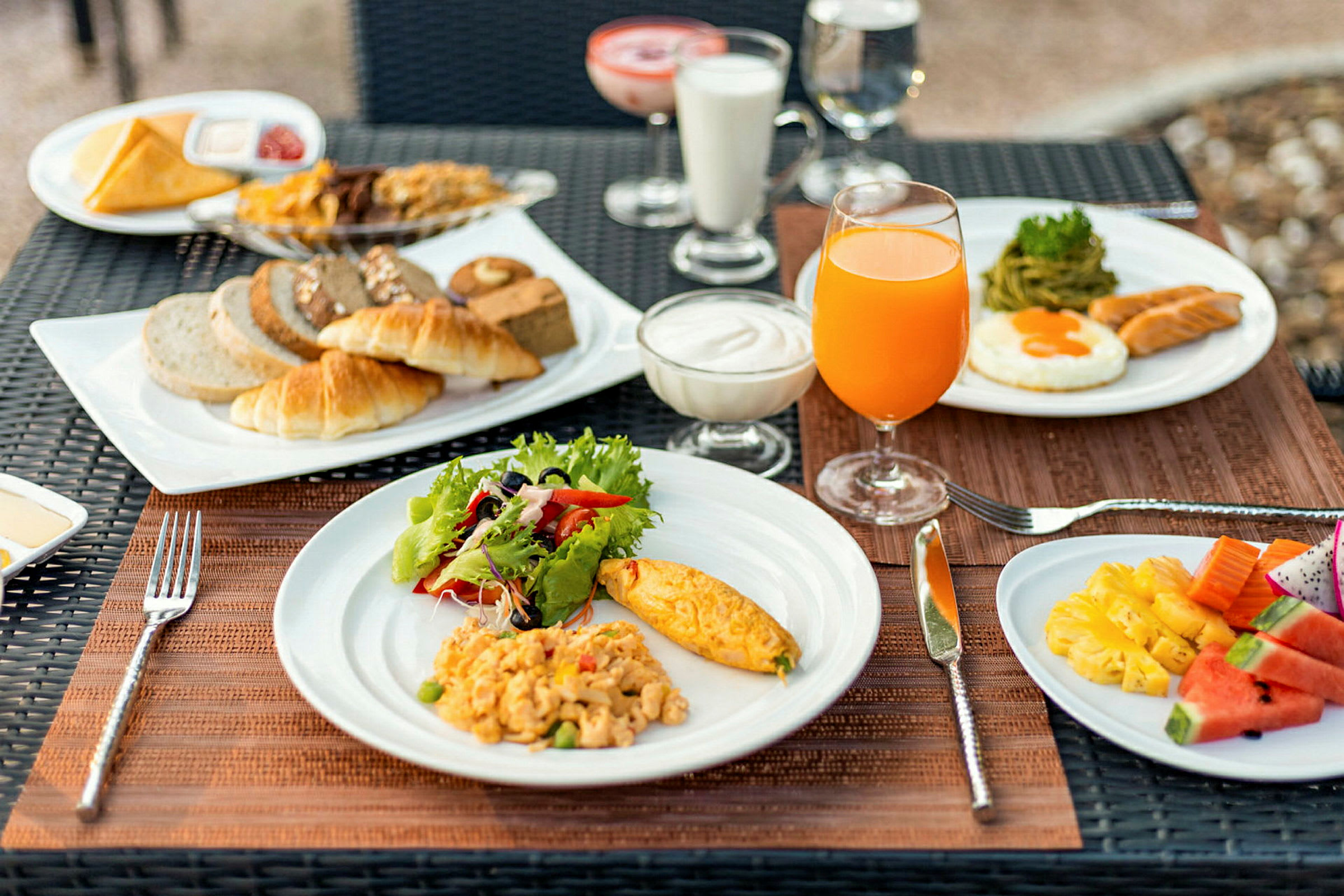 En frukostservering med olika rätter som omelett, sallad, bakverk, juice och frukt, upplagt på tallrikar vid ett bord. (AI-genererad text)