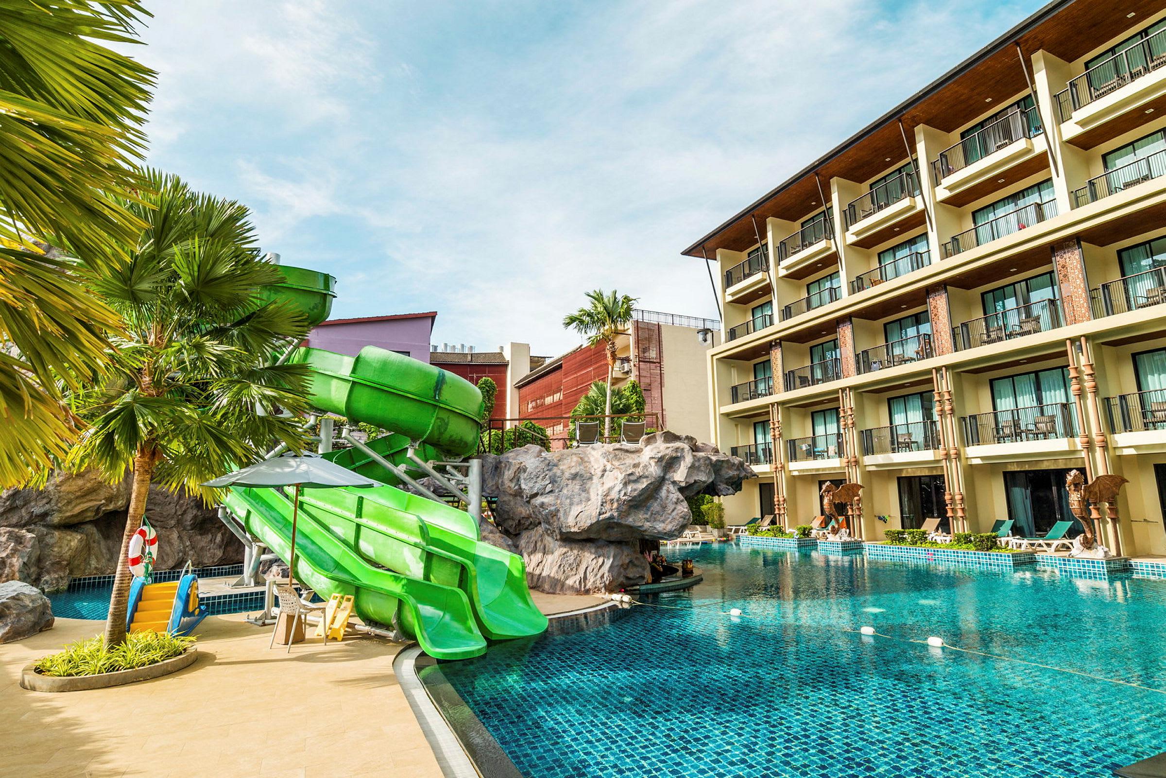 Hotellpool med gröna rutschkanor och en byggnad i bakgrunden. (AI-genererad text)
