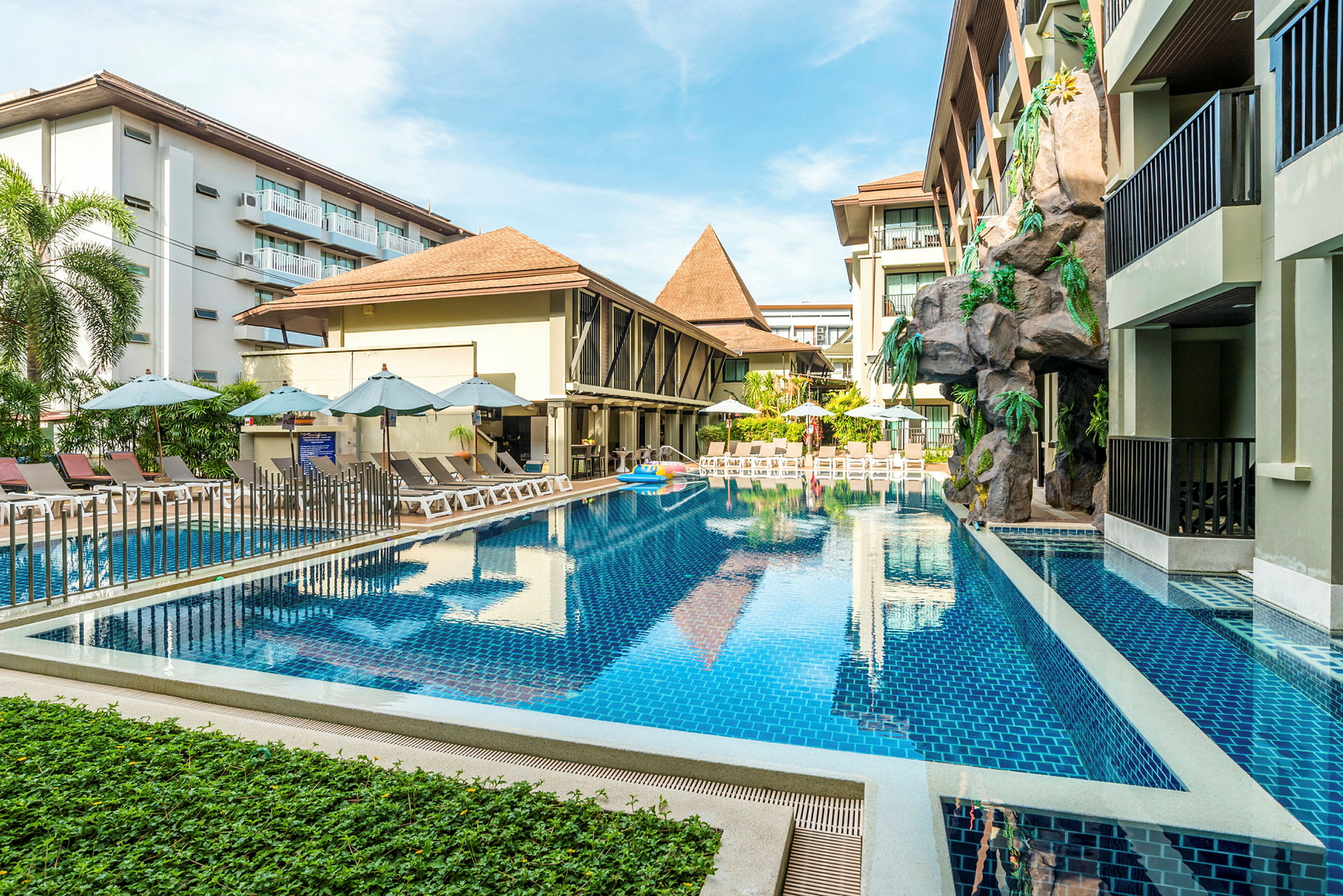 Hotellpool med solstolar och parasoll vid byggnader. (AI-genererad text)