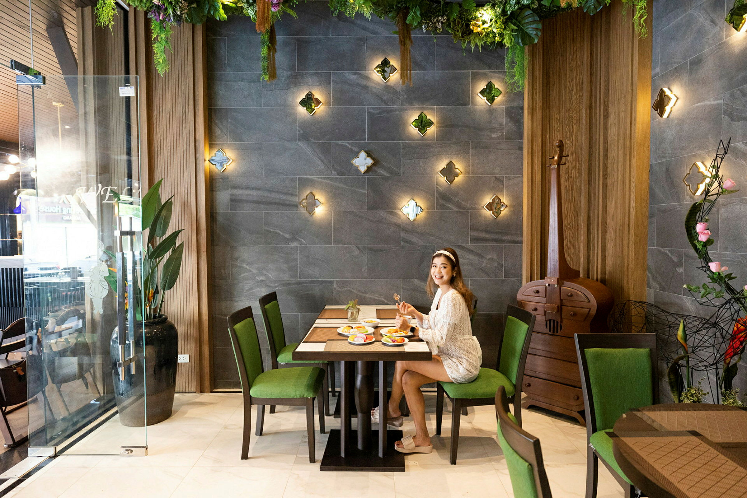 Person sitter vid ett bord på en restaurang med väggdekorationer och grönskande inredning. (AI-genererad text)