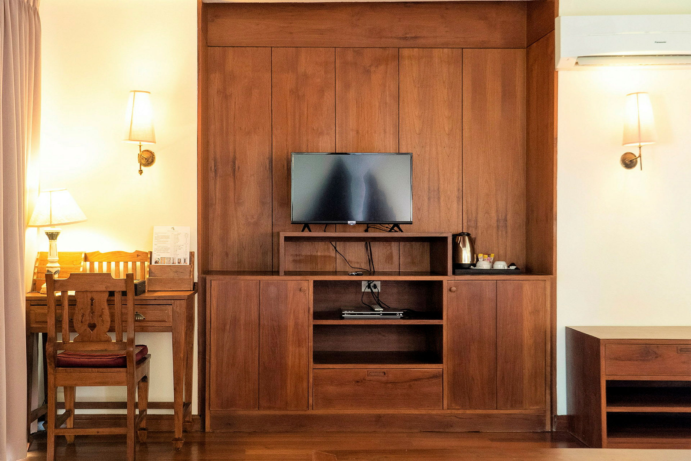 Interiörbild av ett hotellrum med en träpanel där en TV, en kaffekokare och ett skrivbord med stol är placerade. (AI-genererad text)
