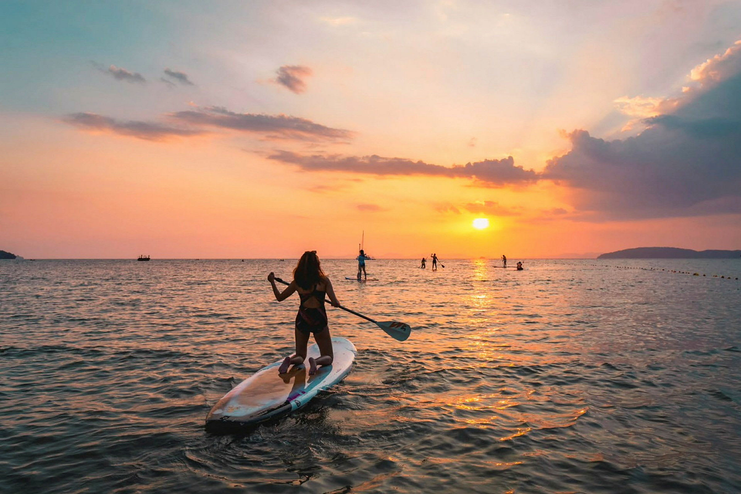 Personer står på paddleboards i havet, med en solnedgång i bakgrunden. (AI-genererad text)