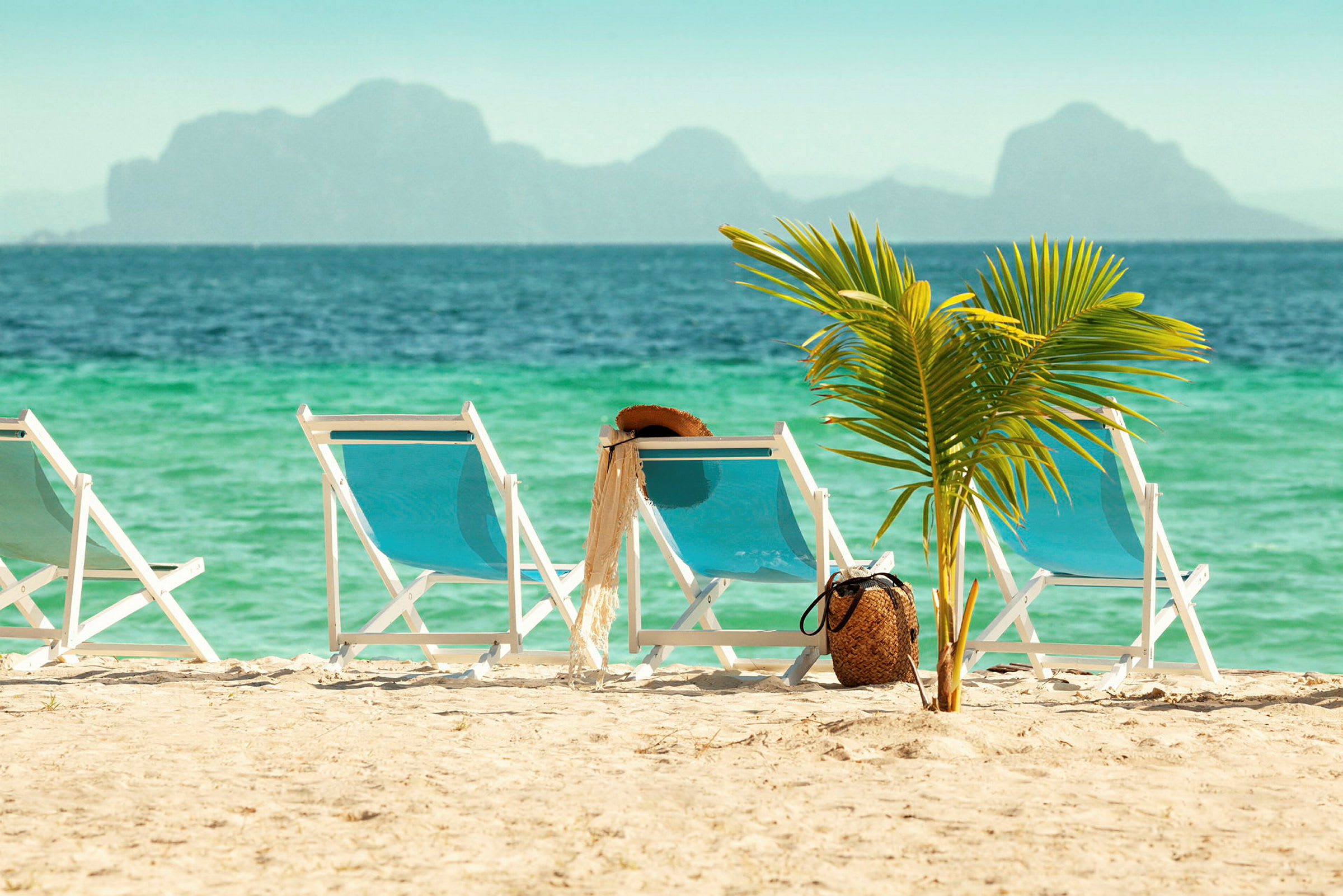 Solstolar på sandstrand med palm och hav i bakgrunden. (AI-genererad text)