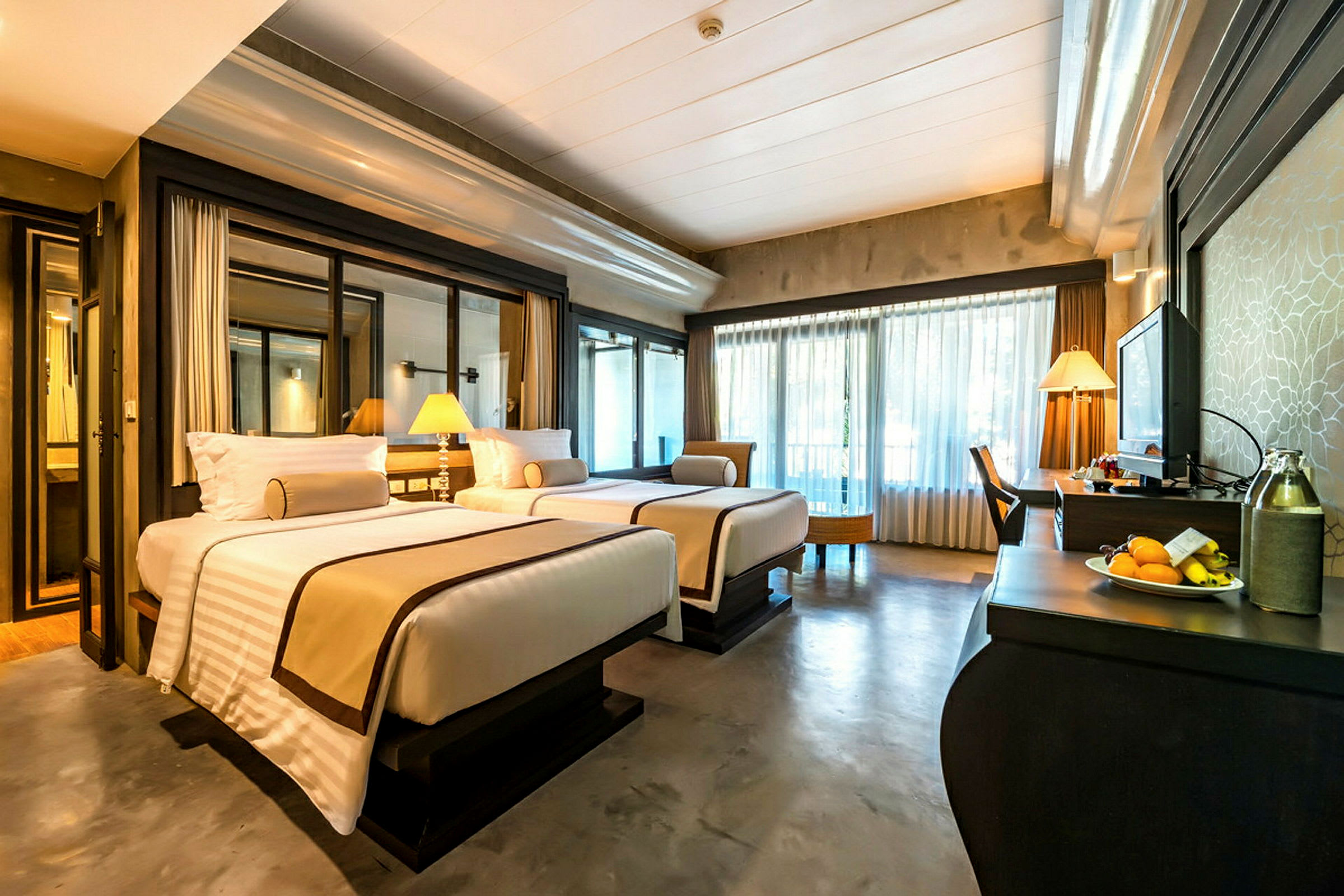Hotellrum med två sängar, skrivbord och stora fönster med genomskinliga gardiner. (AI-genererad text)