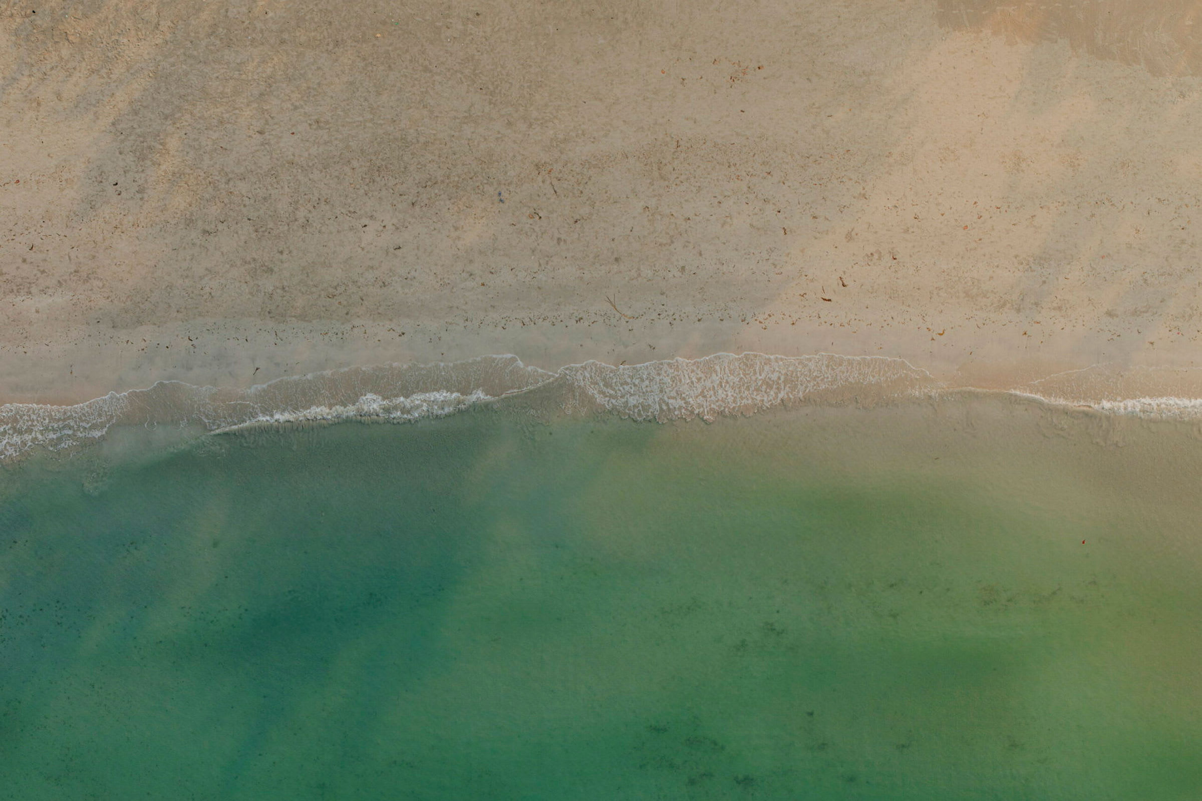 Flygbild av en strandlinje med vågor som rullar in mot sanden och havet i gröna toner. (AI-genererad text)