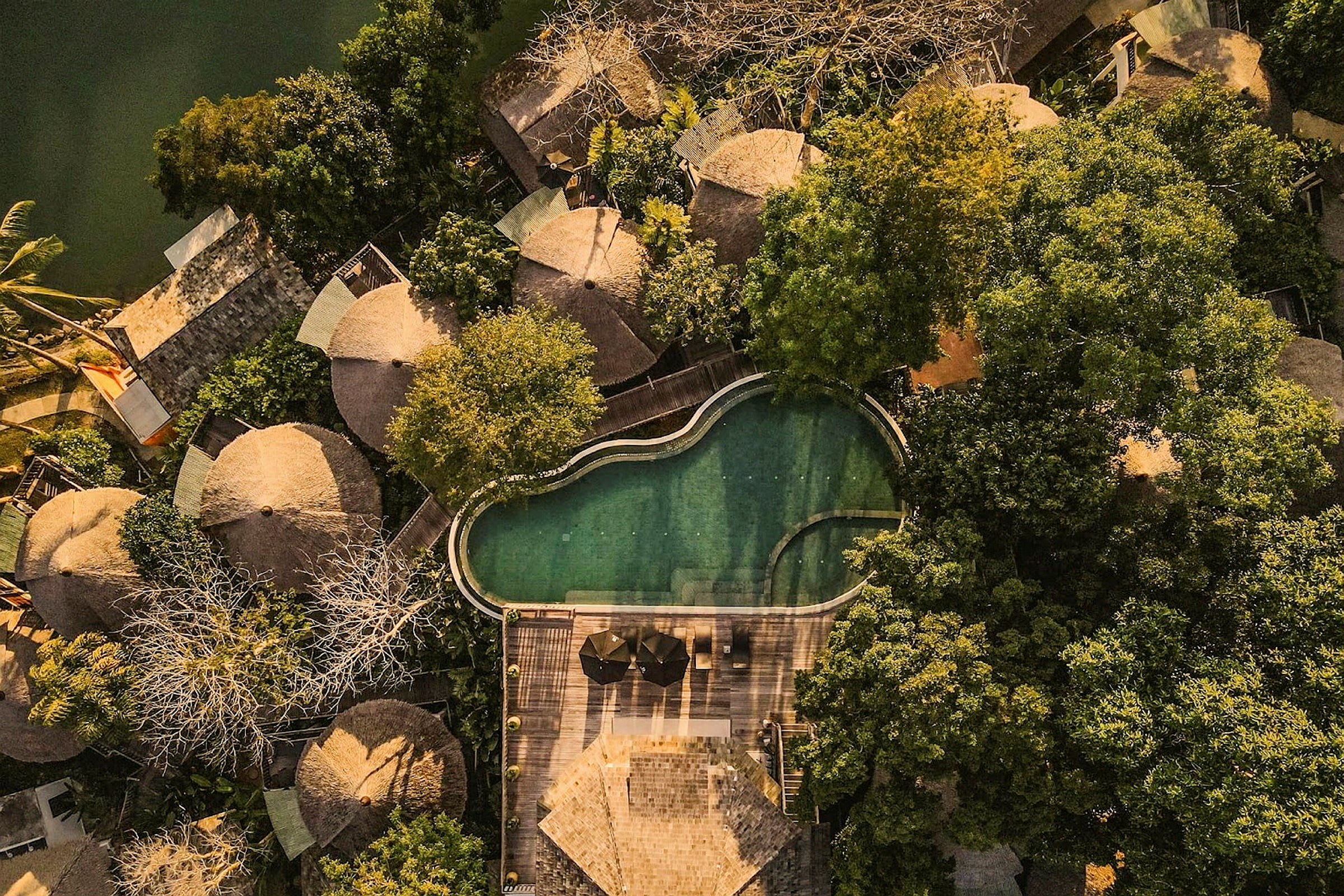 Flygfoto av flera runt formade hus omgivna av frodig grönska, vid sidan av en oregelbunden pool och en träterrass. (AI-genererad text)