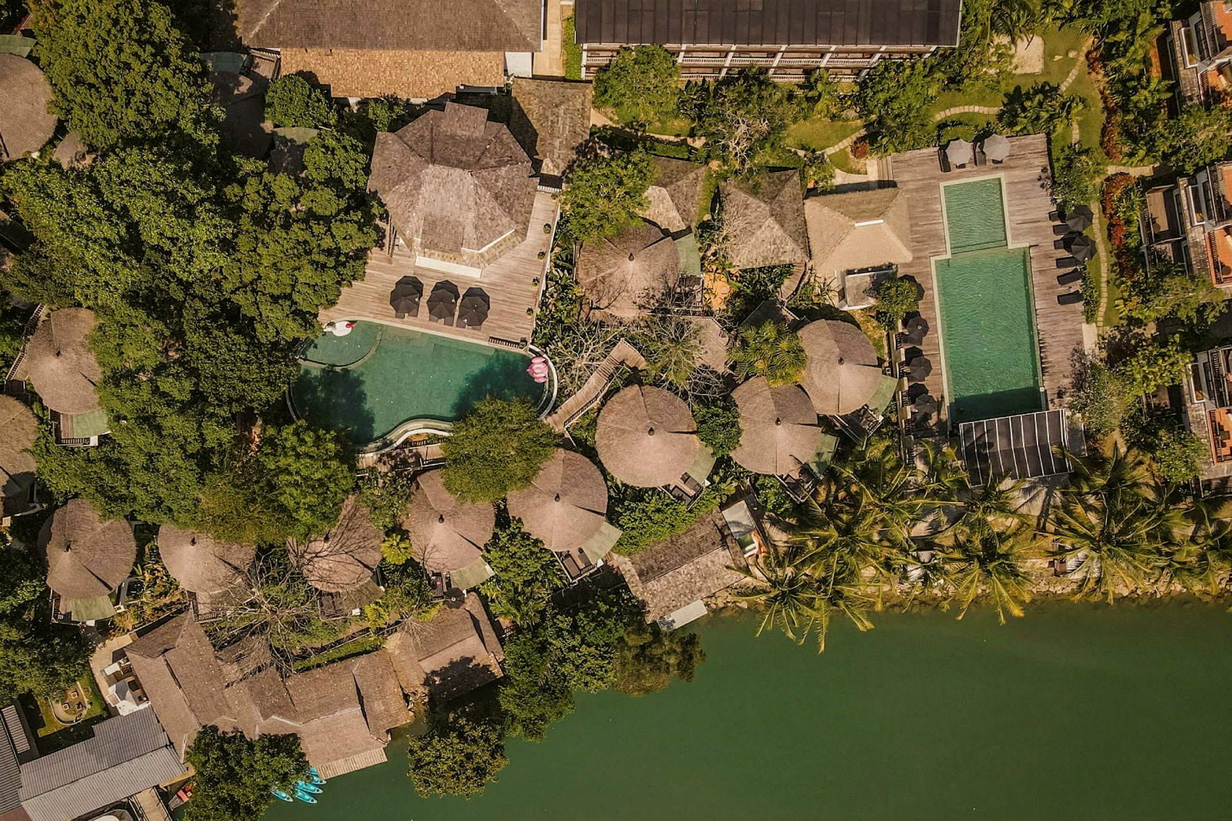 Flygfoto av en resort vid en vattenkälla med pooler, takförsedda byggnader och grönska. (AI-genererad text)