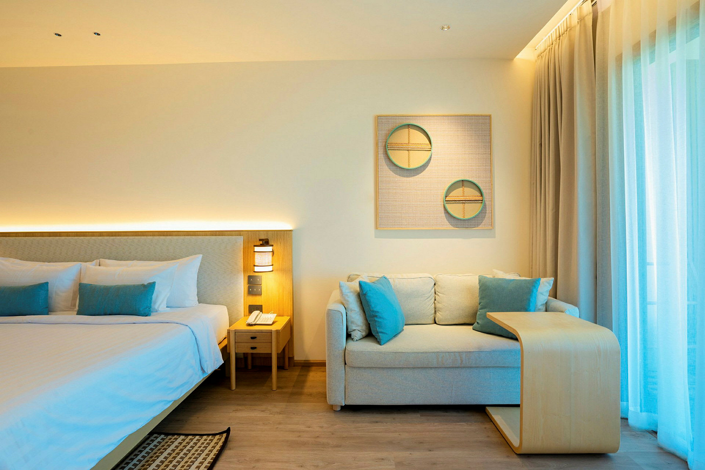 Ett hotellrum med en dubbelsäng, en soffa med kuddar och ett litet träbord. Ljusa gardiner täcker ett fönster i bakgrunden. (AI-genererad text)
