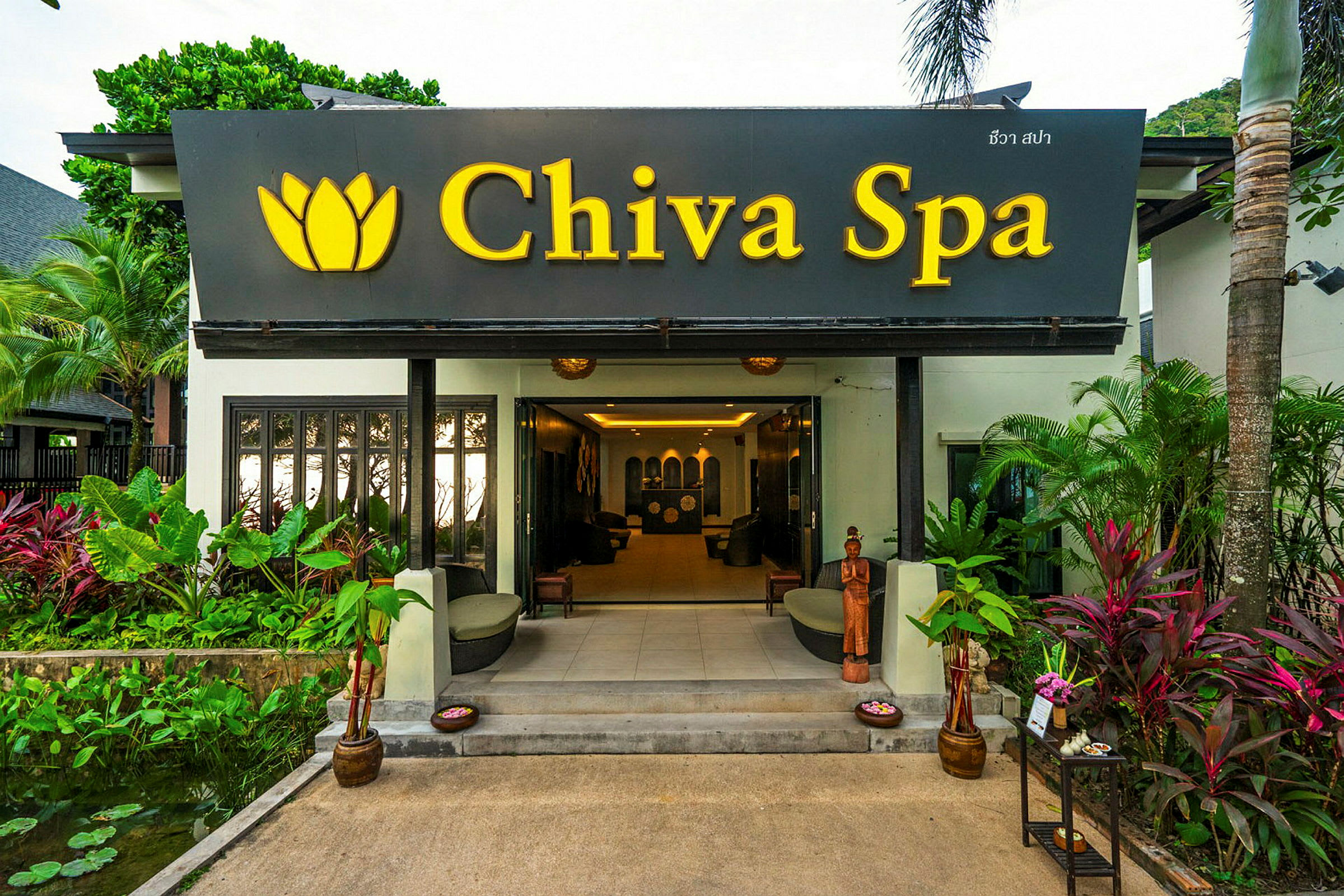 Entrén till en spa-anläggning med skylt med texten "Chiva Spa" och omgivande växter. (AI-genererad text)
