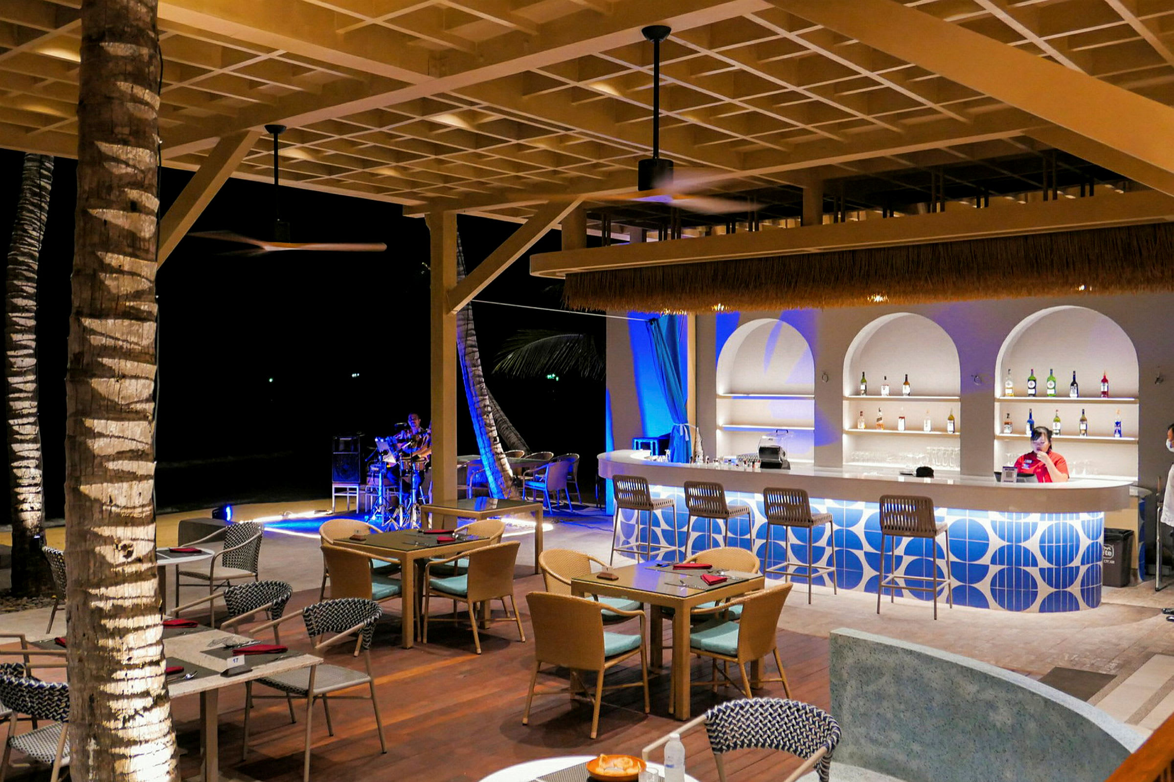 En utomhusbar och restaurang med moderna möbler och en person som spelar musik i bakgrunden. (AI-genererad text)