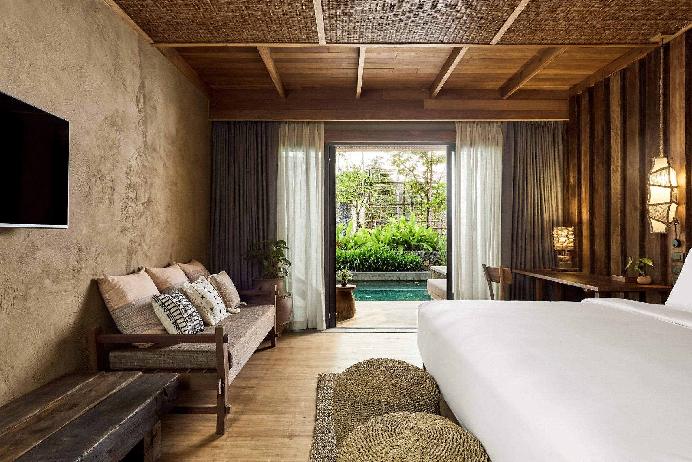 Ett hotellrum med en säng, en soffa och en utsikt mot en privat pool och trädgård. (AI-genererad text)