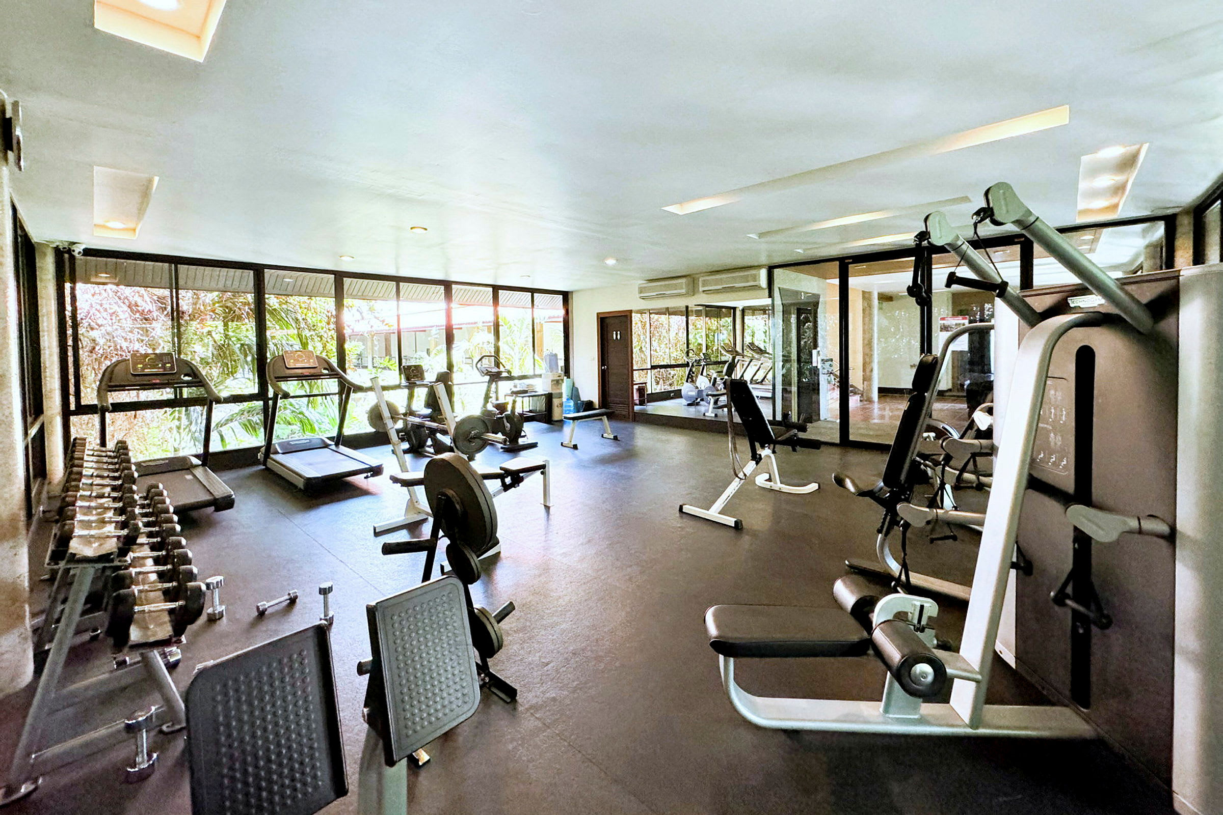 Ett väl belyst gym med träningsutrustning som löpband, styrketräning och hantlar. (AI-genererad text)
