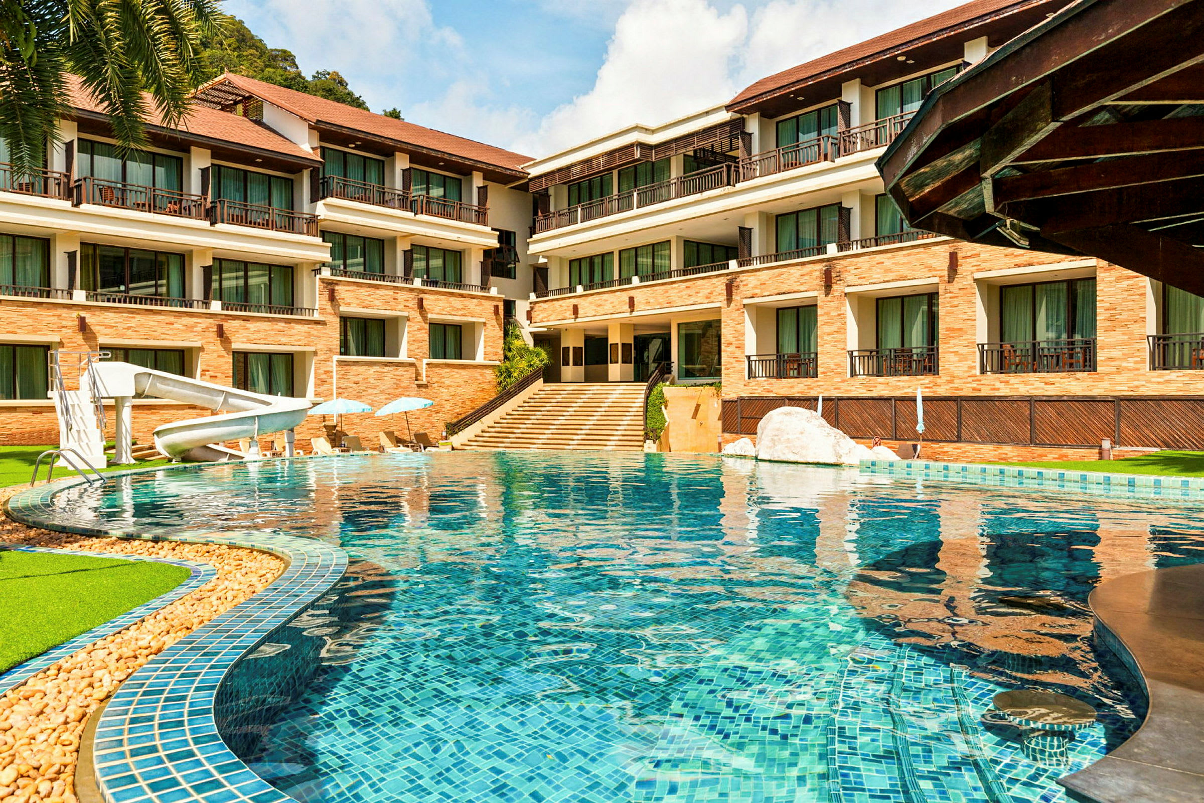 Ett hotell med en pool med vattenrutschbana framför en byggnad med flera våningar av balkonger. (AI-genererad text)