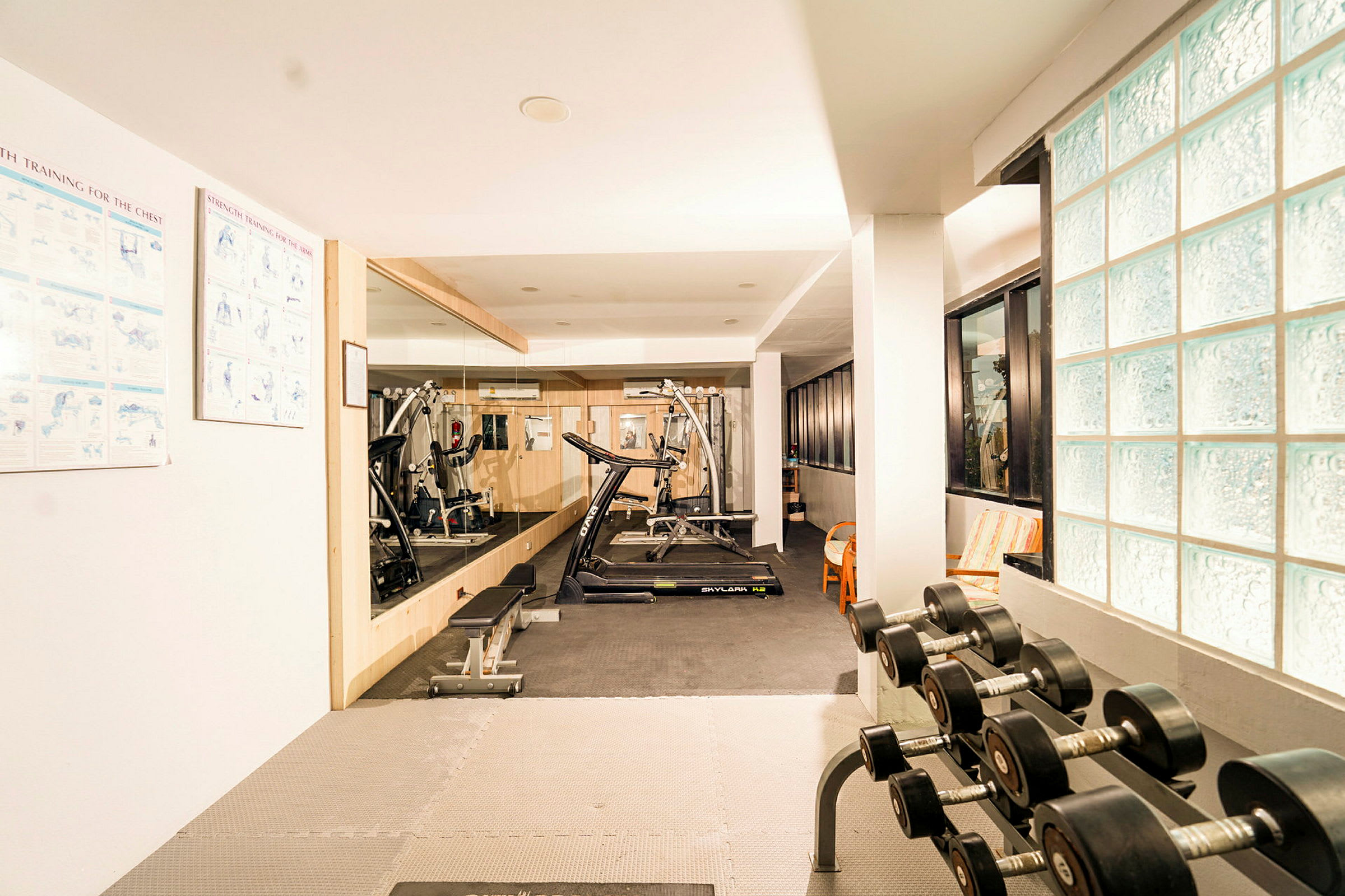 Ett gym med träningsutrustning som löpband, bänkpress och hantlar i en ljus lokal. (AI-genererad text)