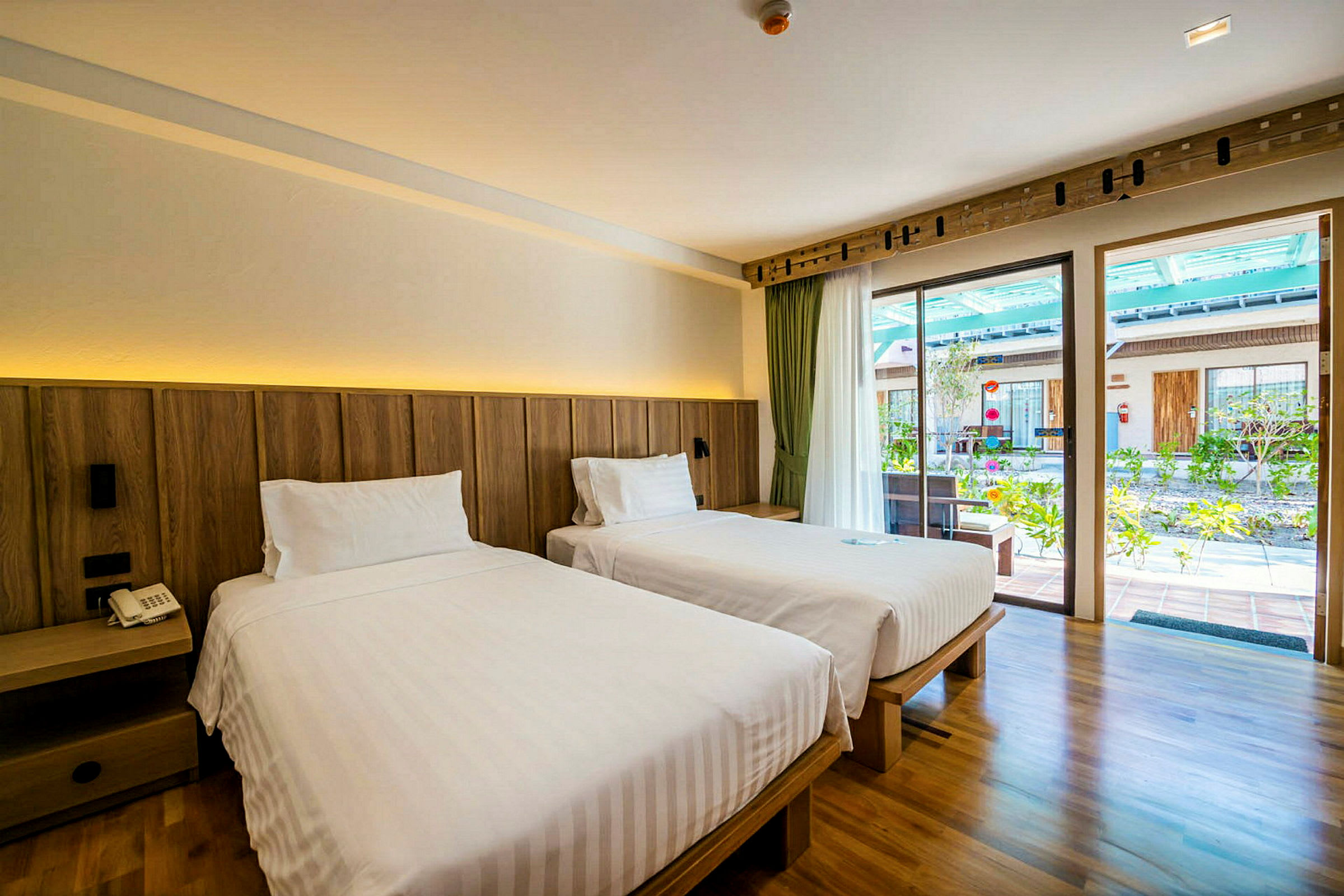 Ett hotellrum med två separata sängar och en utsikt mot en solig uteplats. (AI-genererad text)