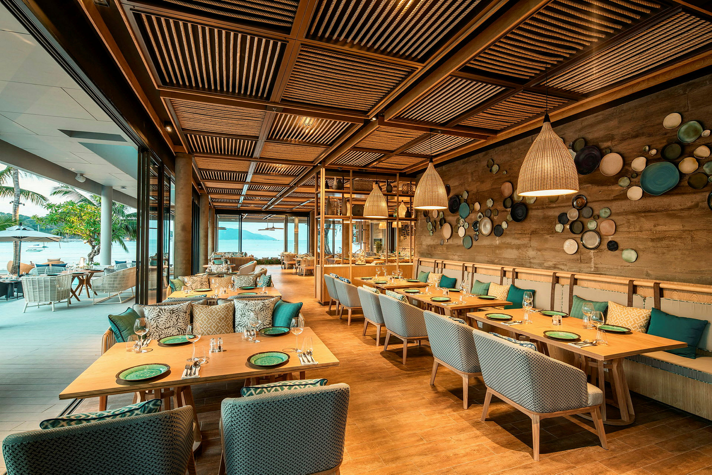 En elegant restaurang med träbord och stolar, dekorerad med moderna lampor och konst på väggarna, med utsikt mot havet. (AI-genererad text)