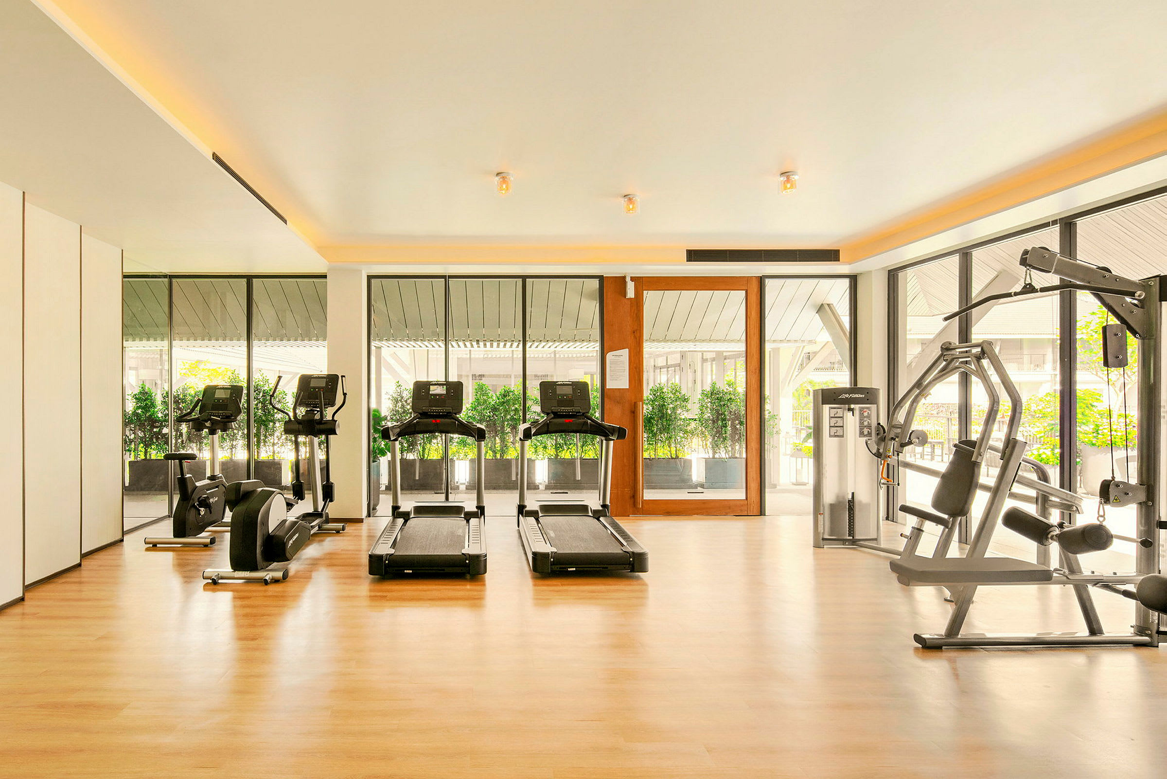 Ett gym med träningsmaskiner, inklusive löpband och styrketräningsutrustning, med stora fönster som släpper in dagsljus. (AI-genererad text)