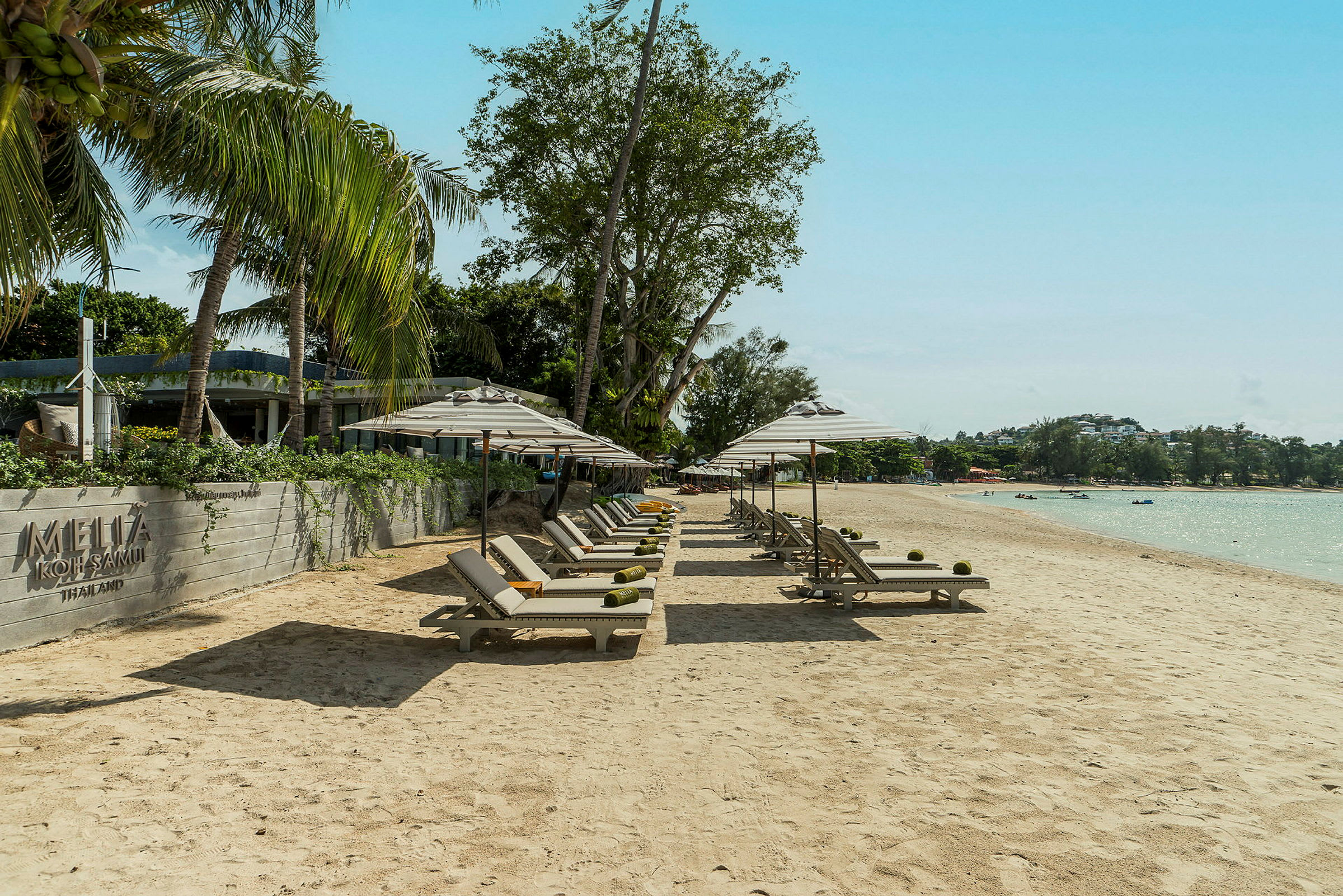 Solstolar och parasoller står uppradade på en sandstrand vid ett hotellområde. (AI-genererad text)