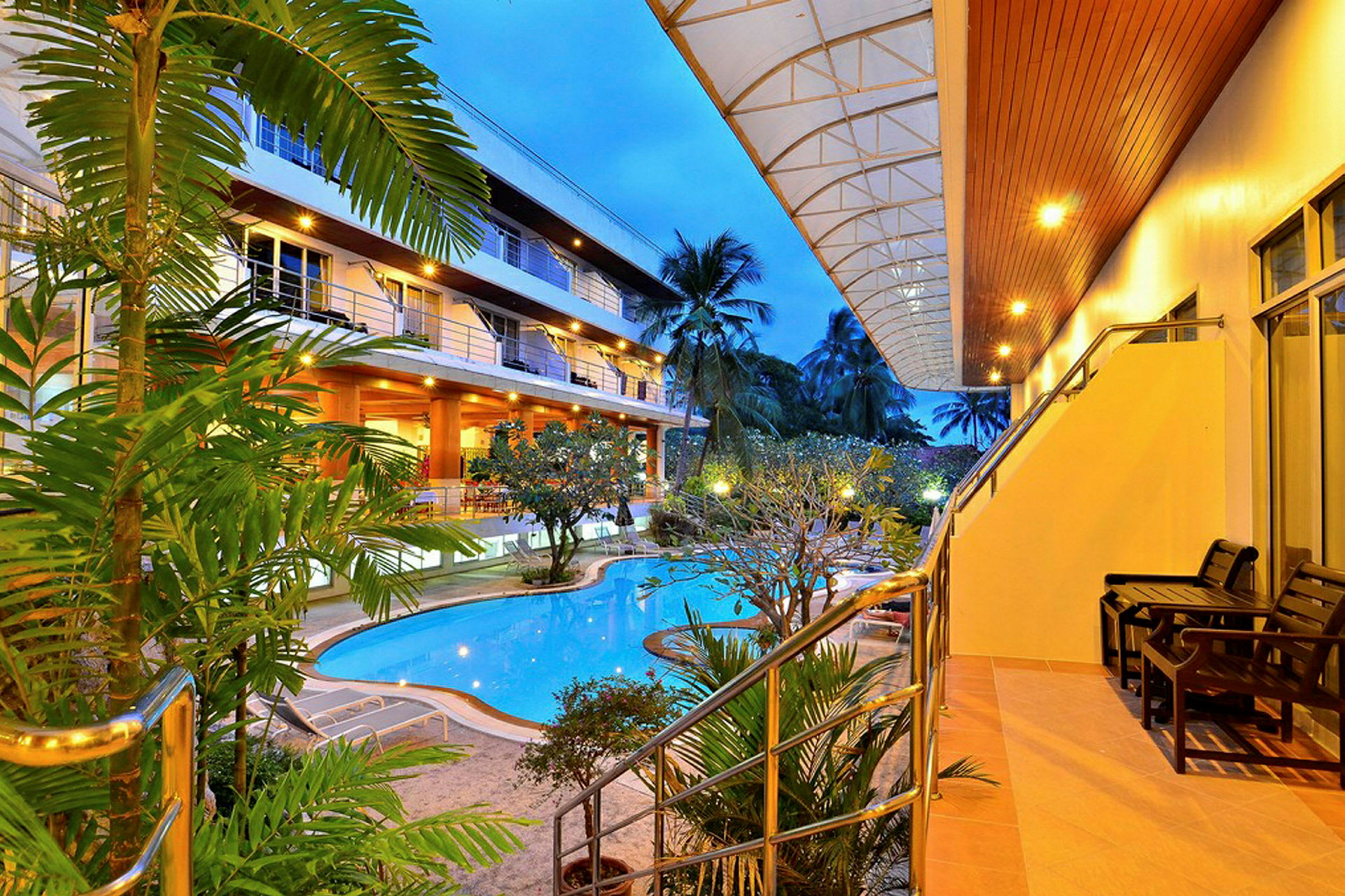Bild av ett hotellområde med en pool omgiven av växter och belysning i kvällsljus. (AI-genererad text)