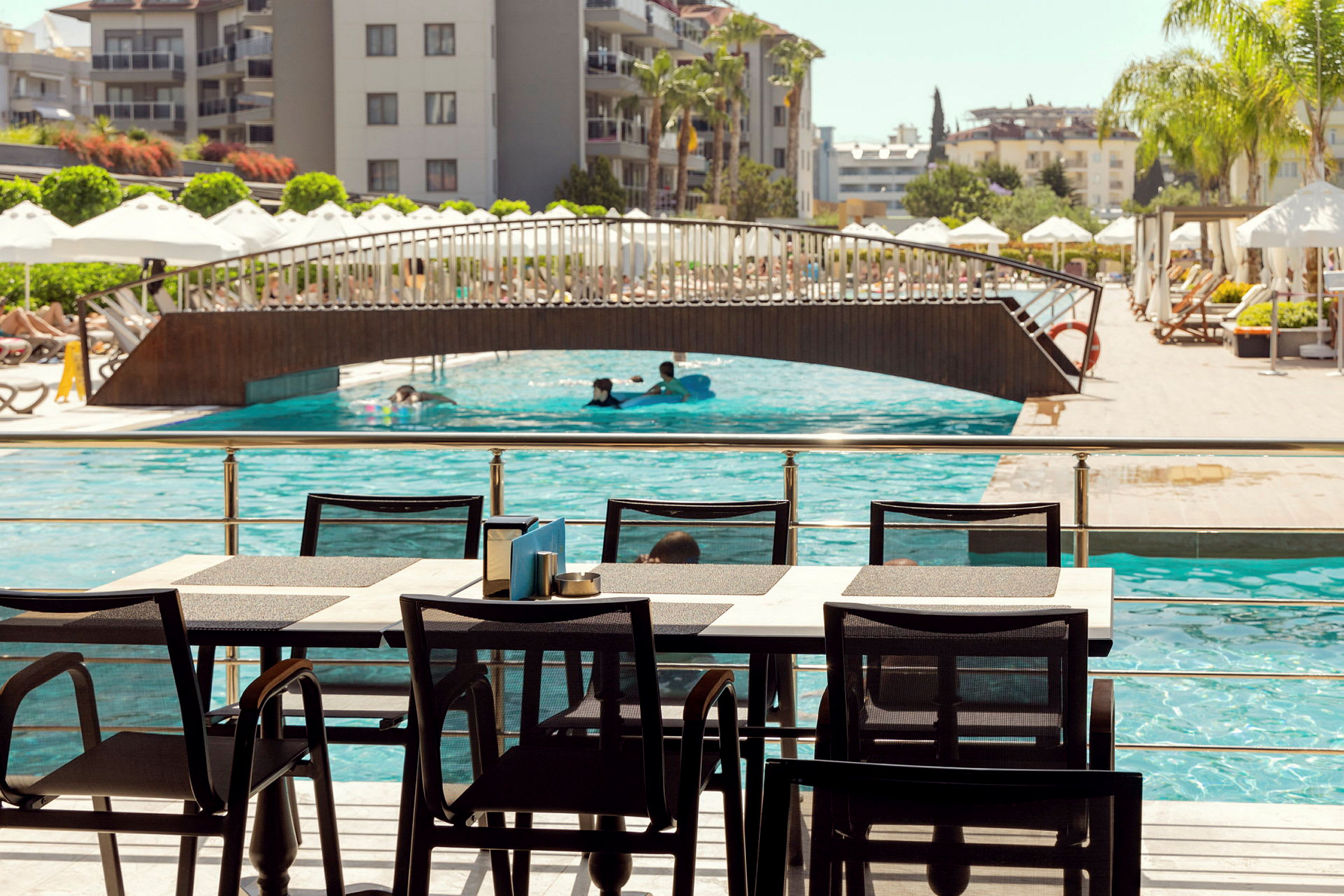 Matplats vid en pool med bro och hotell i bakgrunden. (AI-genererad text)