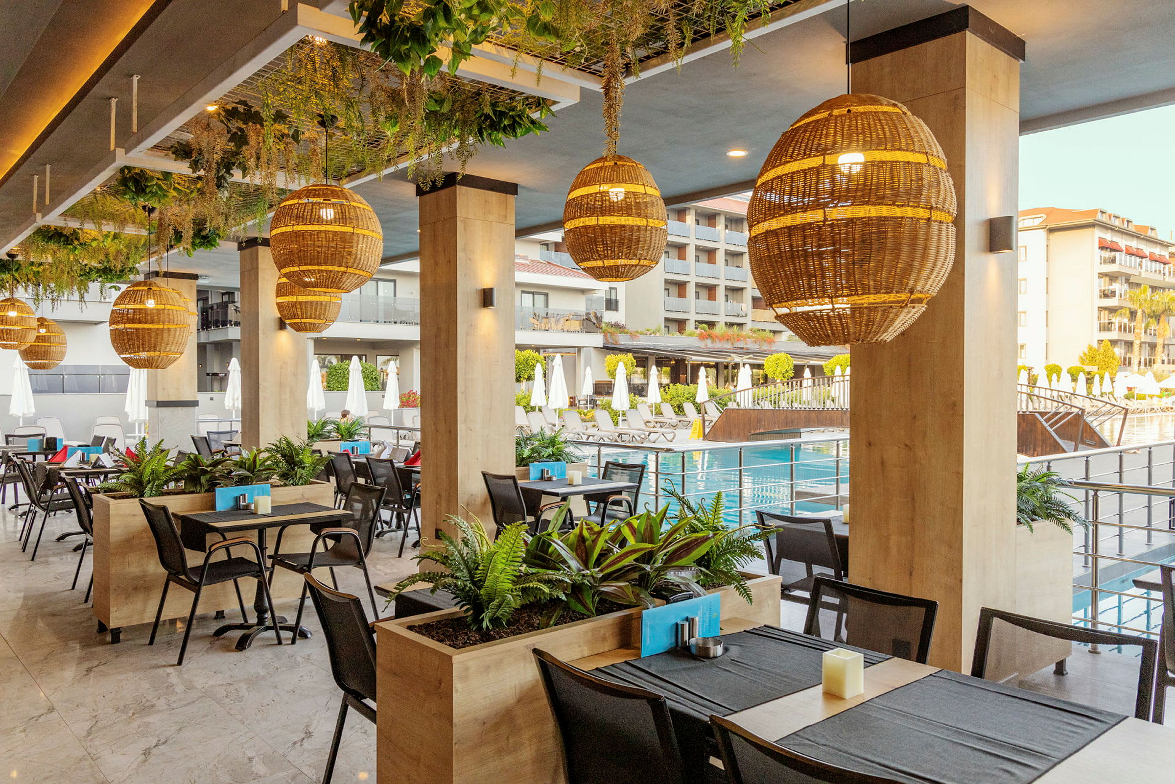 Restaurangområde med sittplatser intill poolen, dekorerat med gröna växter och stora, runda lampor. (AI-genererad text)