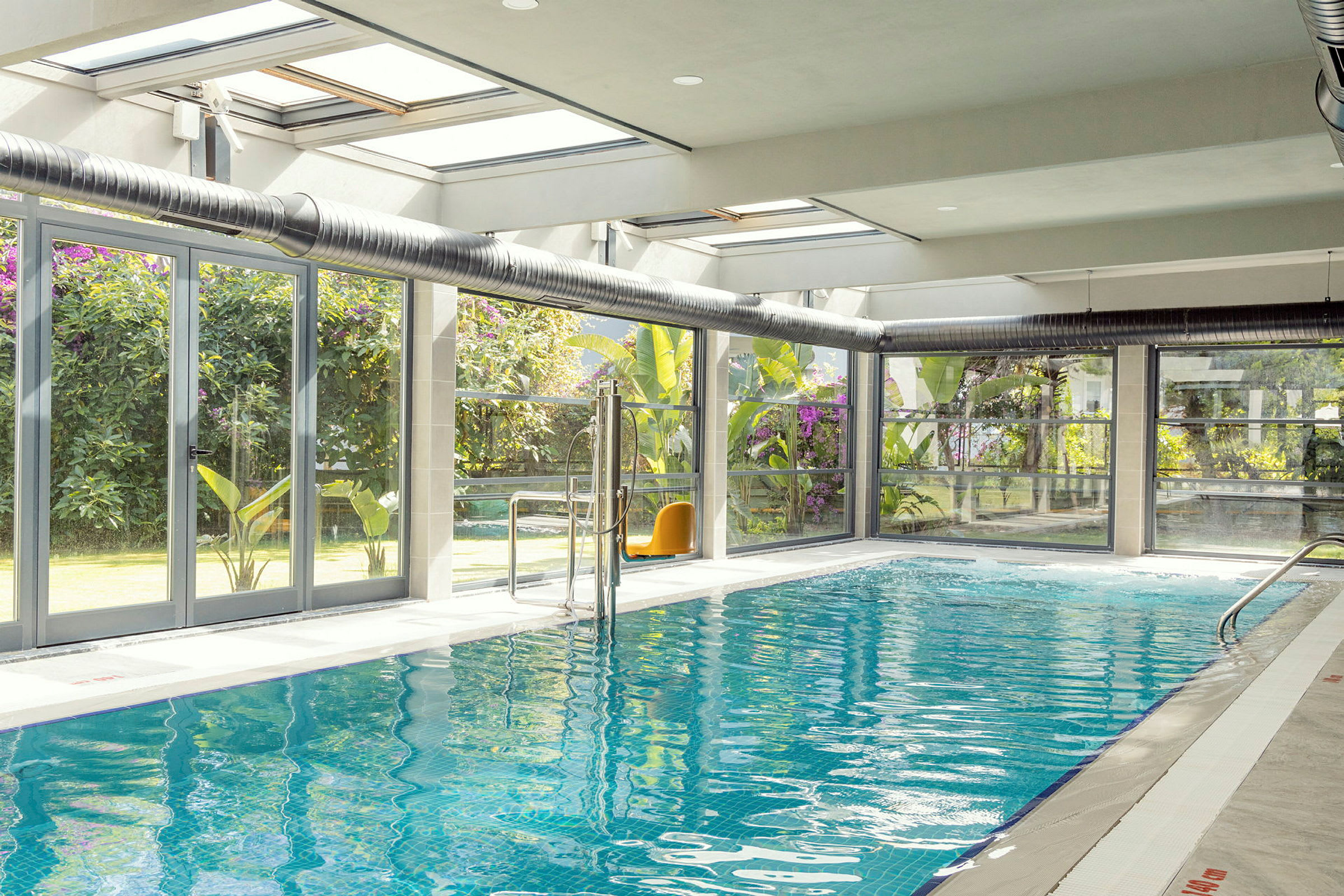 Inomhuspool med glasväggar och utsikt mot trädgården. (AI-genererad text)