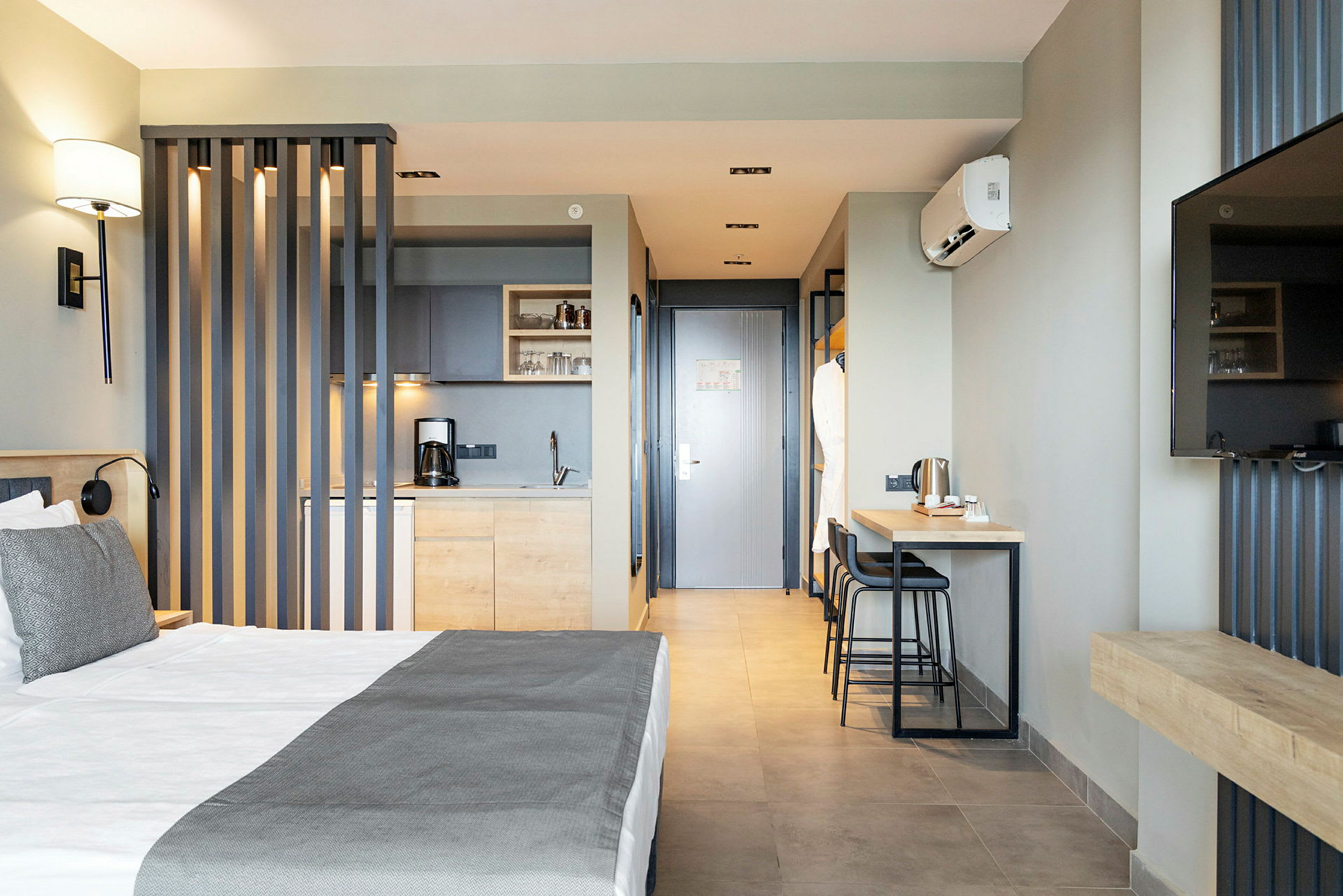 Ett hotellrum med en säng, ett minikök, bord med stolar och en tv. (AI-genererad text)