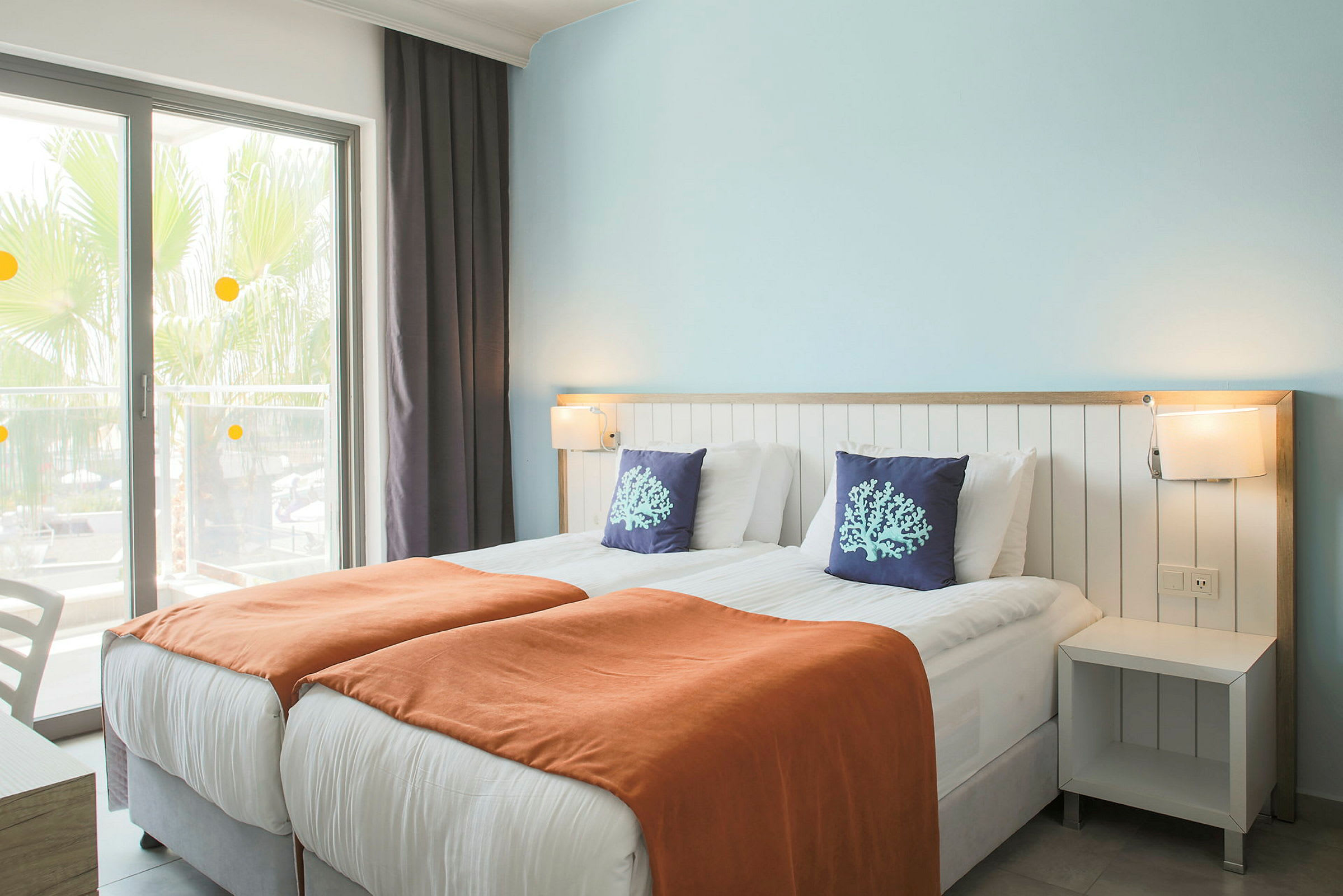 Hotellrum med två enkelsängar, orange filtar och dekorativa kuddar. (AI-genererad text)